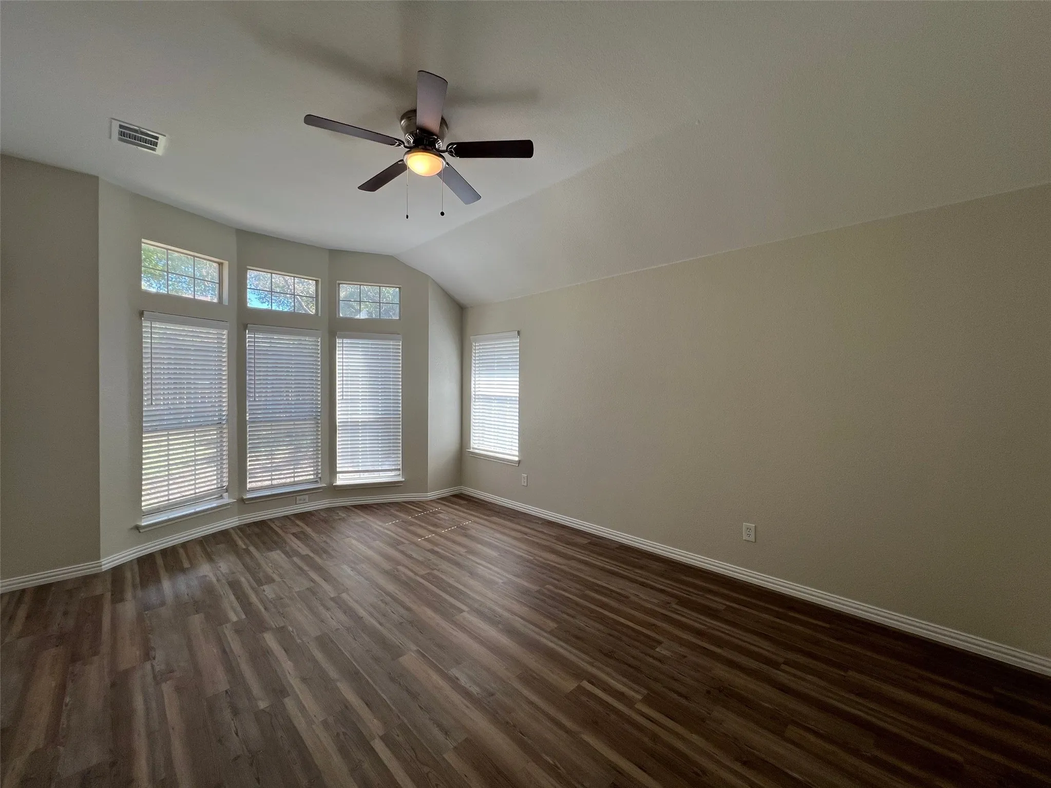 Vaulted ceilings featuring a central ceiling fan, wood-finish flooring, and a bay window configuration with multi-pane windows
