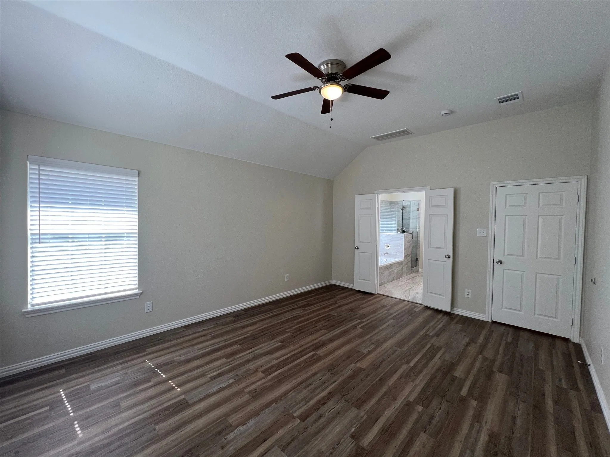Vaulted ceiling with an integrated multi-blade ceiling fan, wood-finish flooring, and double doors opening to a tiled interior space
