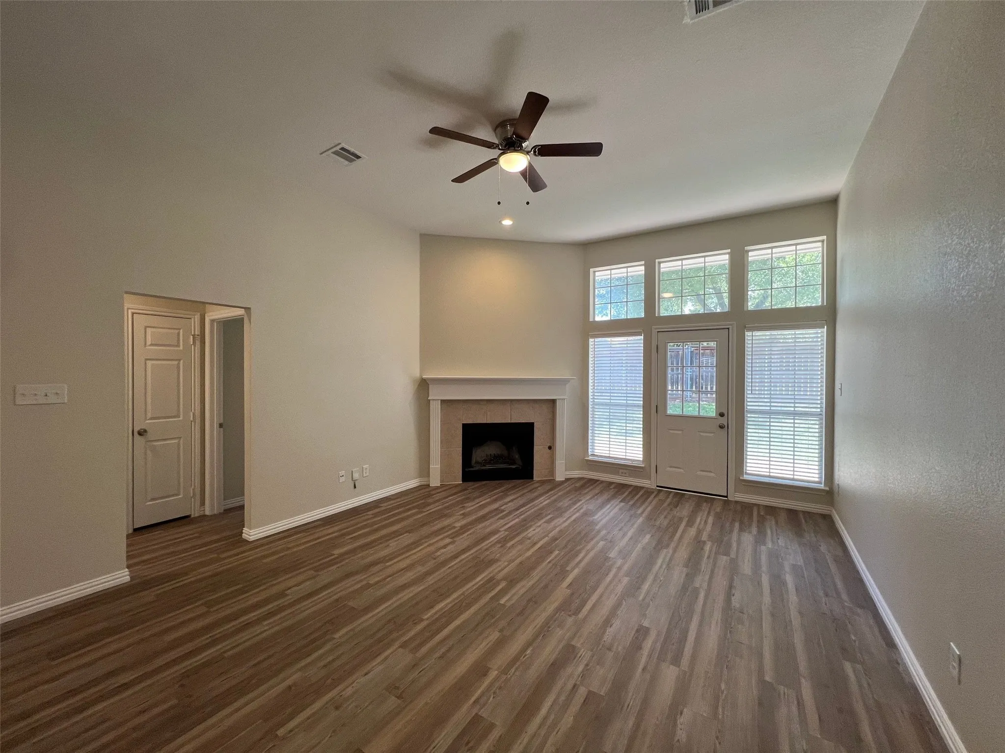 Living area featuring high ceilings, wood-finish flooring, a fireplace with a mantel, and large windows with an integrated glass-paneled door