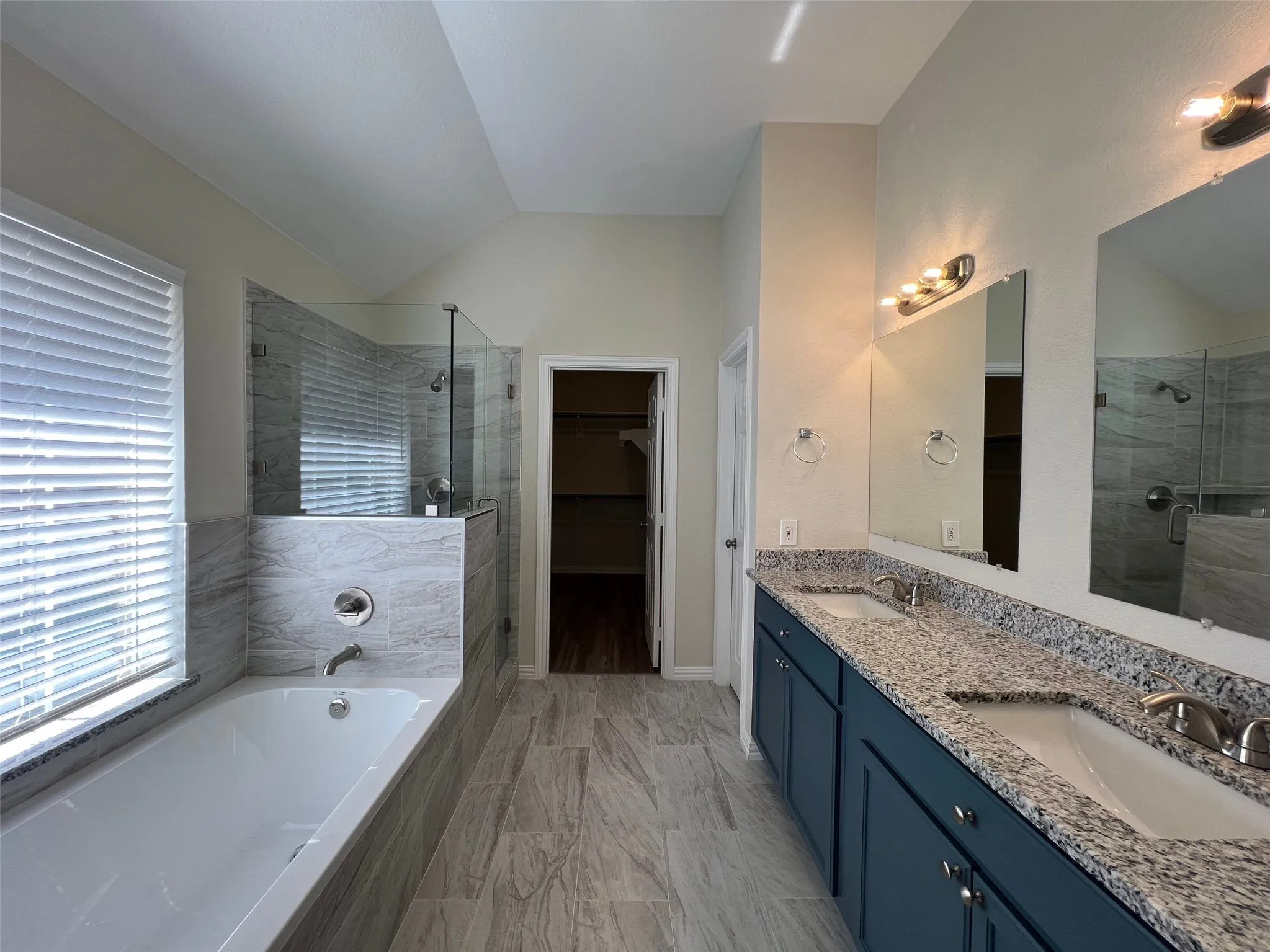 Bathroom featuring a dual-sink vanity with stone-finish countertops, deep-basin drop-in sinks, a tiled soaking tub, and a separate glass-enclosed shower with tiled surround