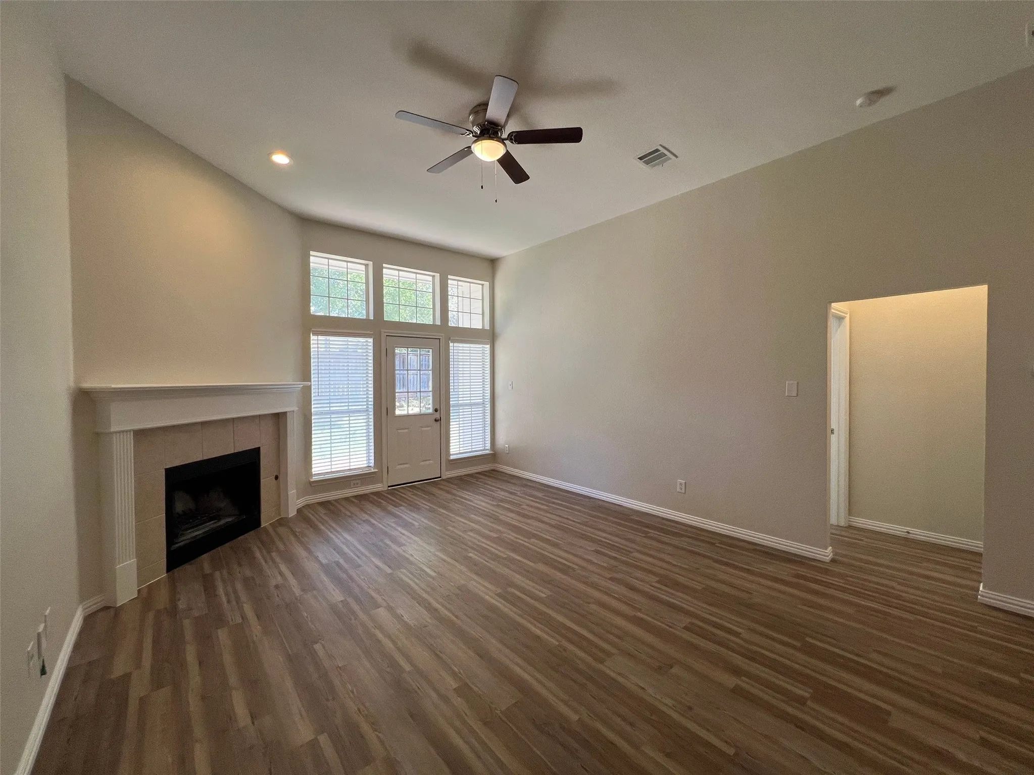 Vaulted ceilings featuring a central overhead fan, wood-finish flooring, fireplace with a custom mantle, and oversized windows providing natural light