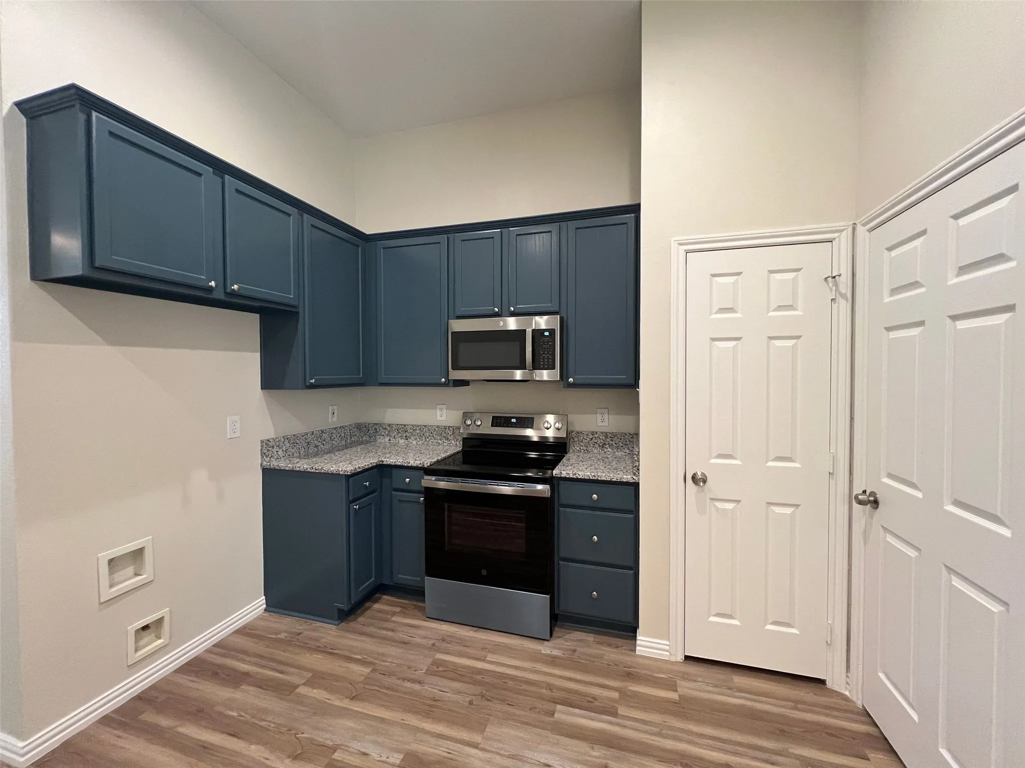 Blue cabinetry with brushed nickel hardware, stone-patterned countertops, stainless steel microwave, built-in electric range, and wood-finish flooring