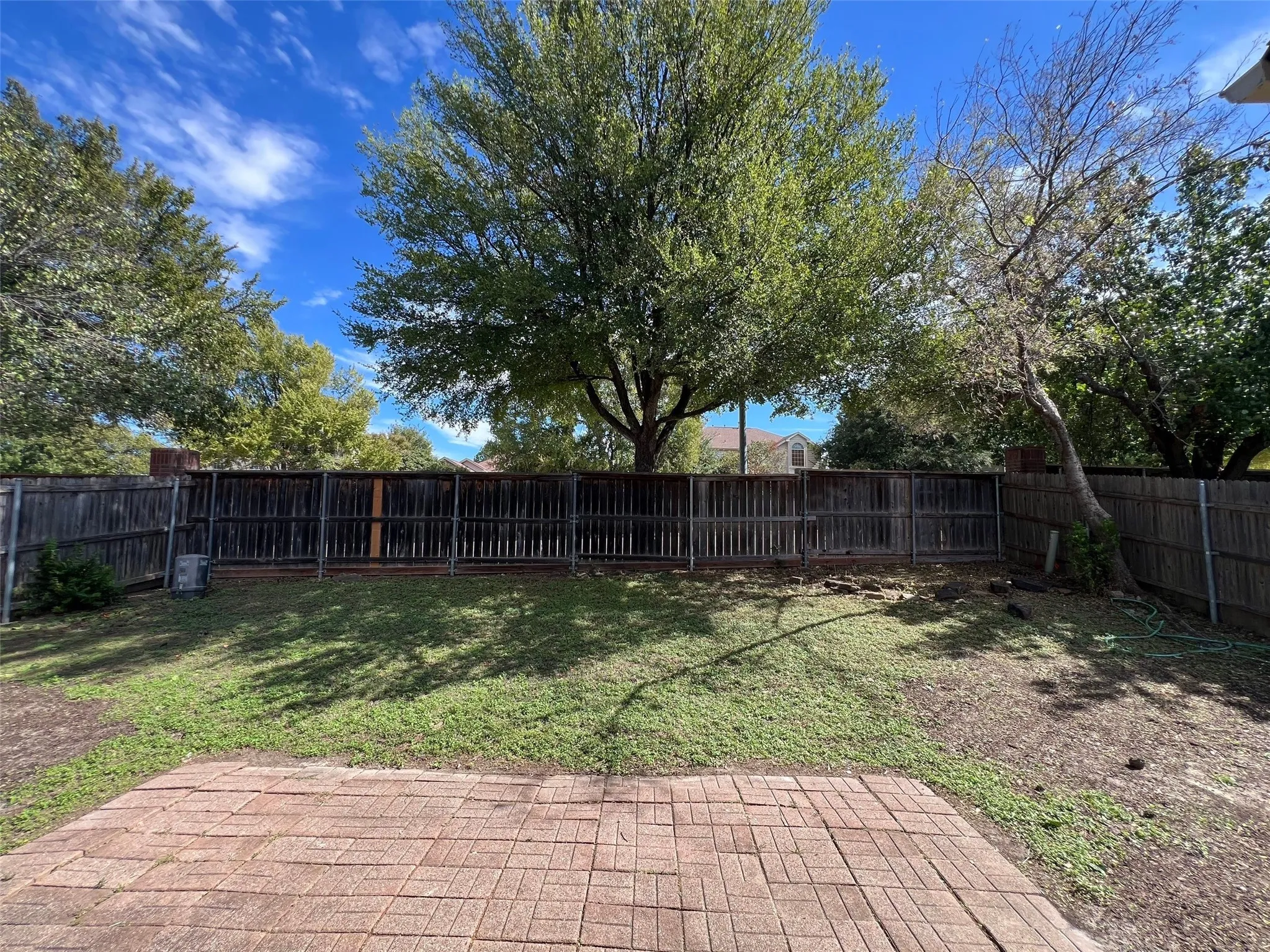 Backyard featuring a brick paver patio, wood privacy fencing, and mature trees