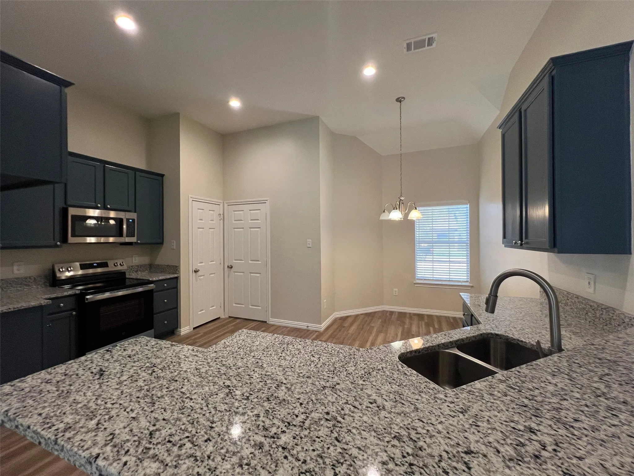 Kitchen featuring dark cabinetry, stone-finish countertops, stainless steel appliances, double-basin undermount sink with a high-arch faucet, and wood-finish flooring