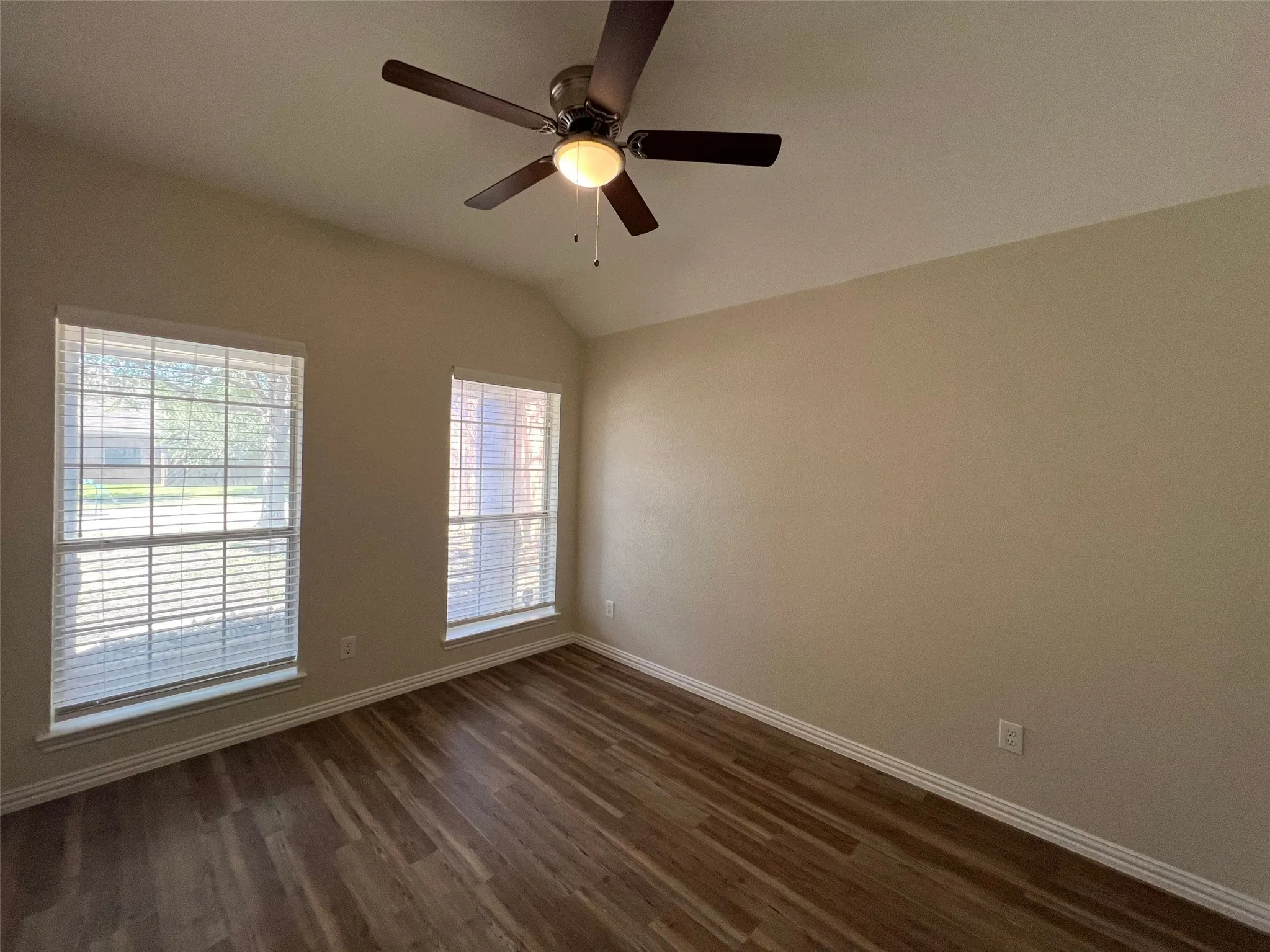 Room featuring vaulted ceilings, wood-finish flooring, two large windows with grid detailing, and a ceiling fan with integrated lighting