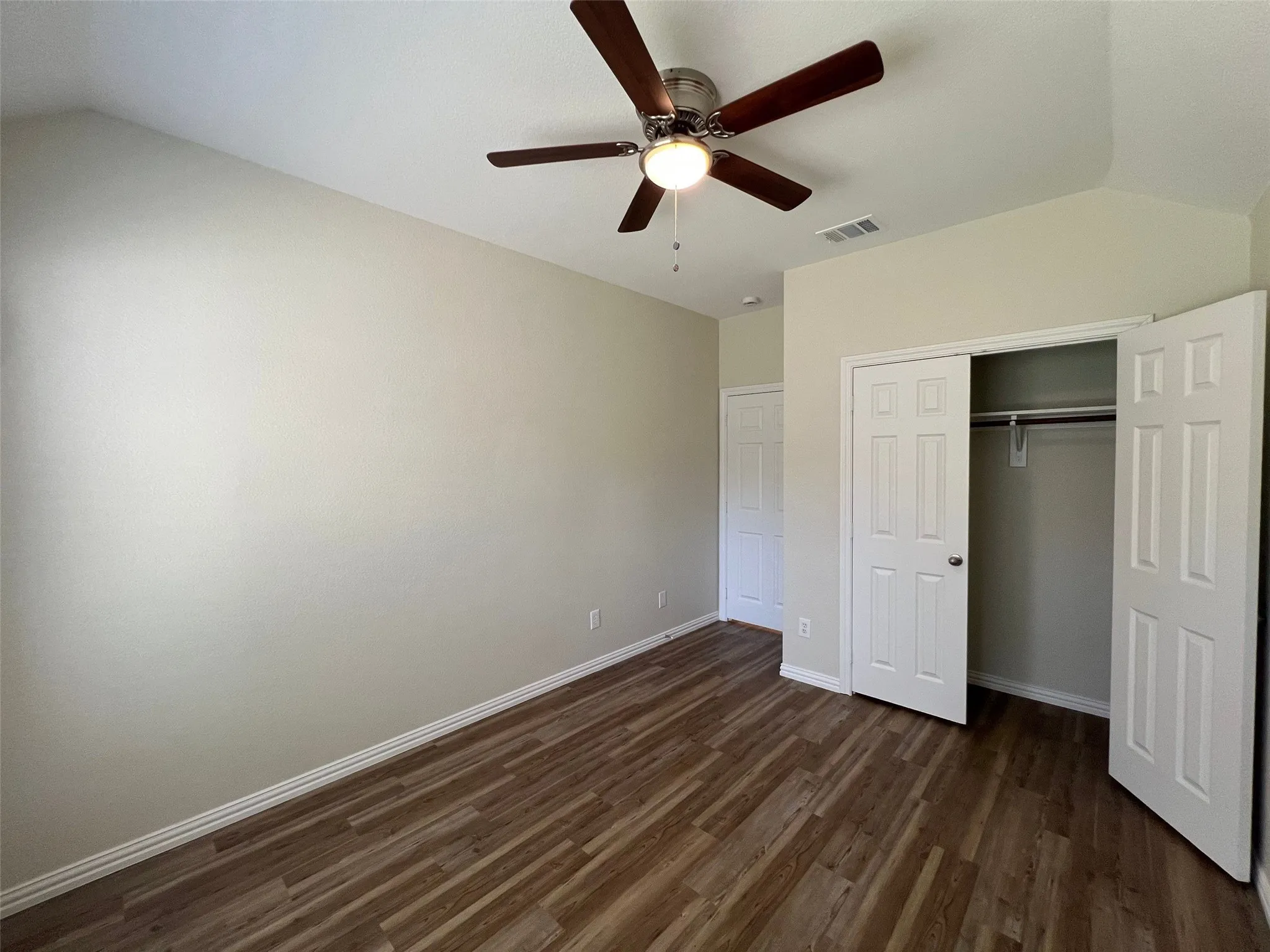 Vaulted ceiling featuring a central wood-blade ceiling fan with integrated lighting, complemented by wood-finish flooring and a double-door closet with internal shelving