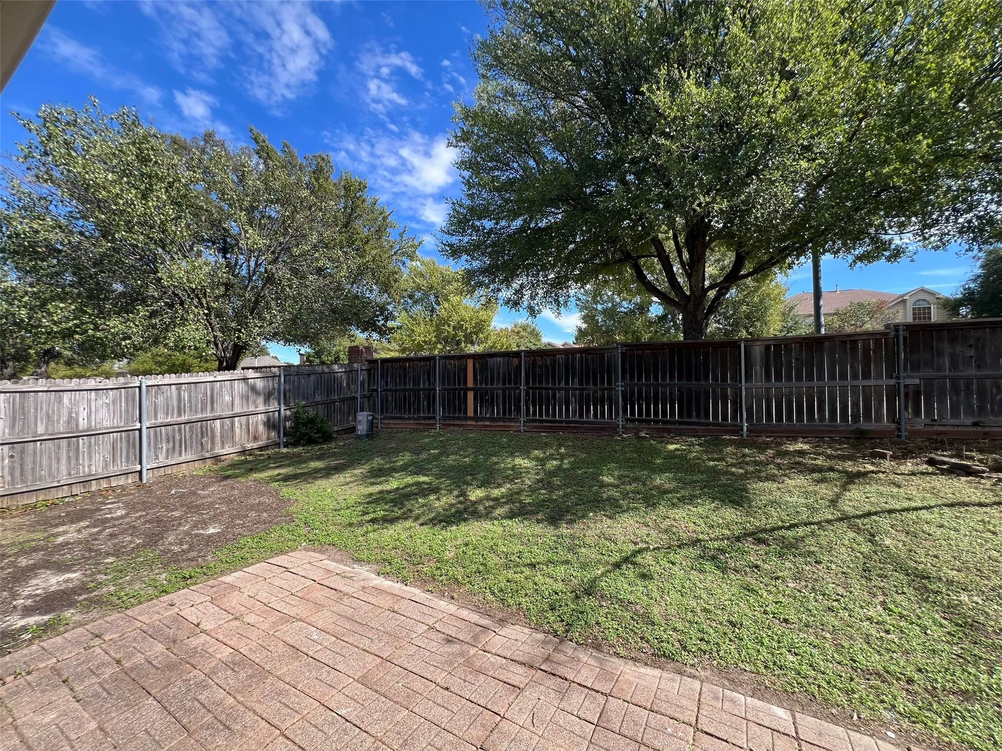 Rear exterior featuring a brick paver patio, wood-slat privacy fencing, and mature trees