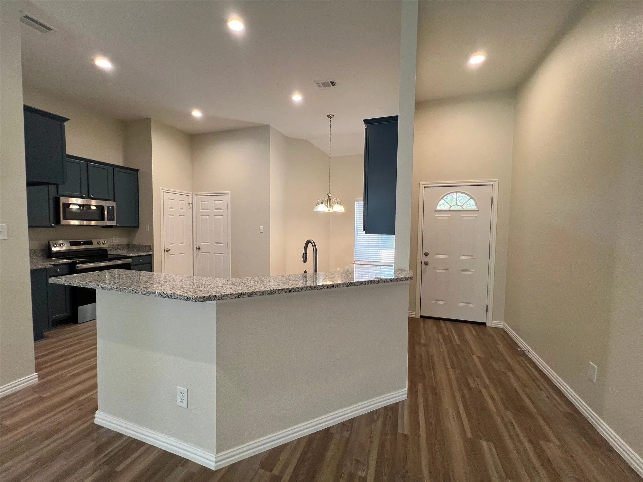 Kitchen featuring dark-toned cabinetry, stone-surface breakfast bar, stainless steel appliances, recessed ceiling lighting, and wood-finish flooring