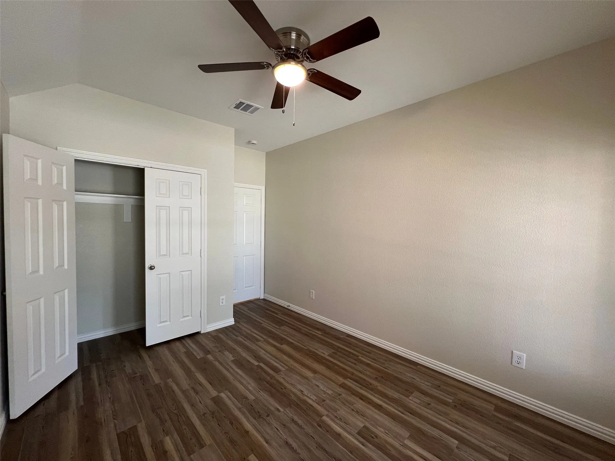 Wood-finish flooring, vaulted ceiling, multi-blade ceiling fan, and six-panel interior doors with reach-in closet