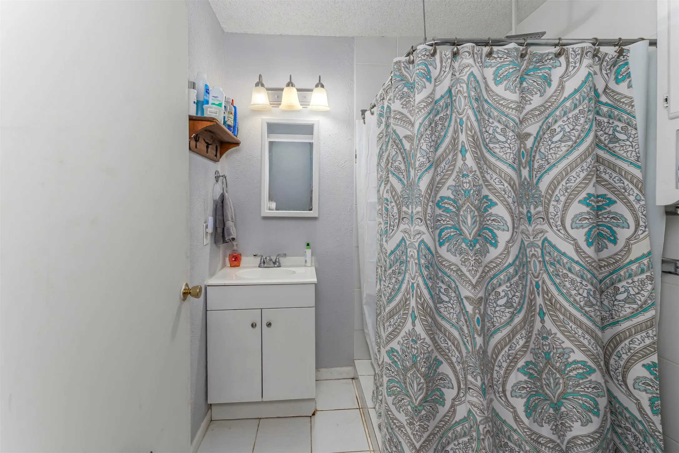 Bathroom featuring a white vanity cabinet with an integrated sink, three-light wall-mounted fixture, recessed medicine cabinet, and tiled flooring