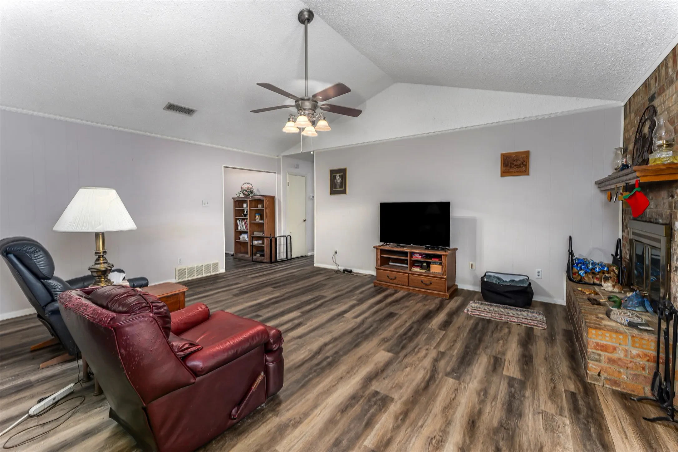 Vaulted ceilings, wood-finish flooring, and a brick-faced fireplace with a wood mantel