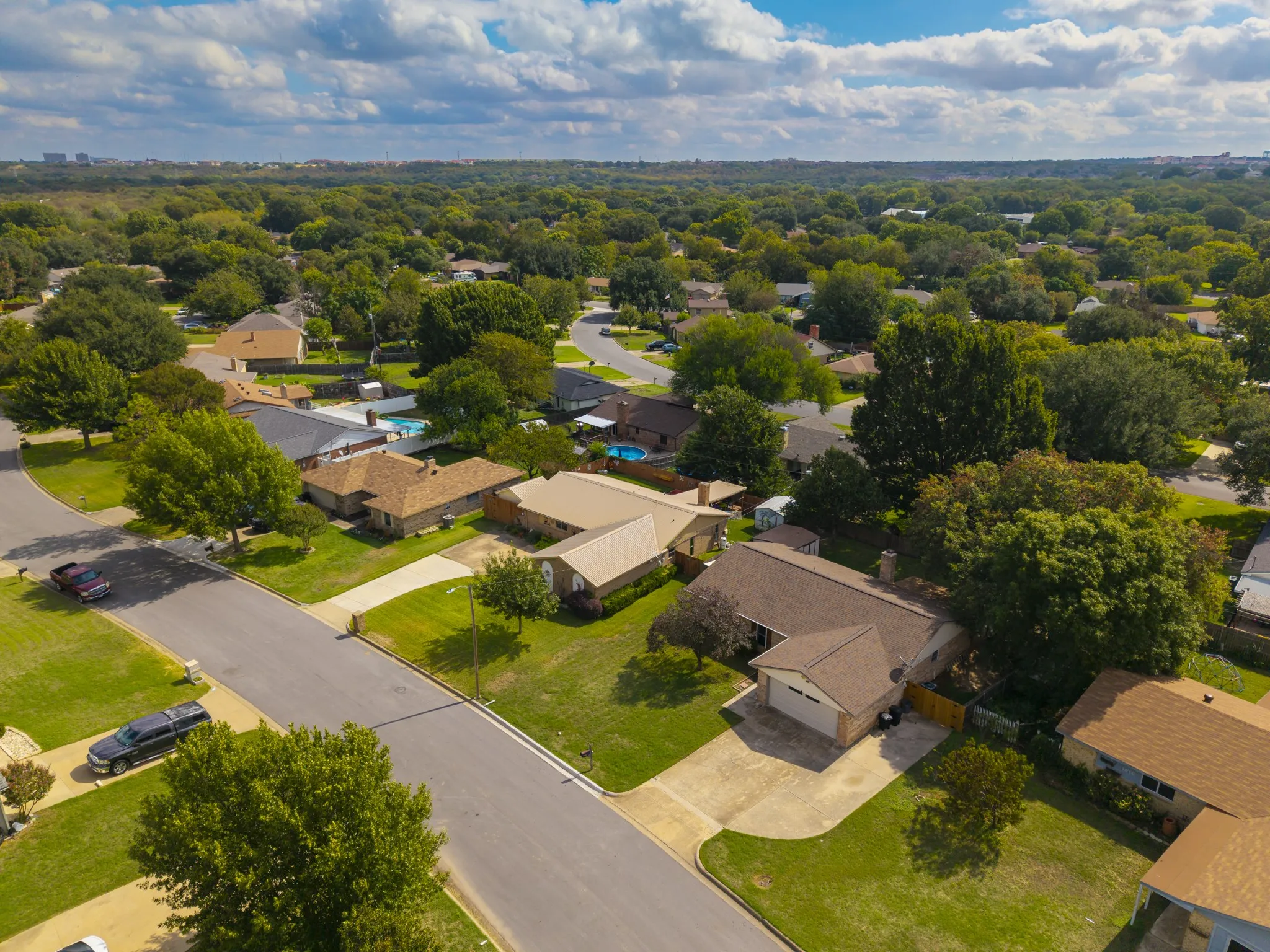 Aerial perspective featuring established residential landscaping, mature trees, and concrete driveways