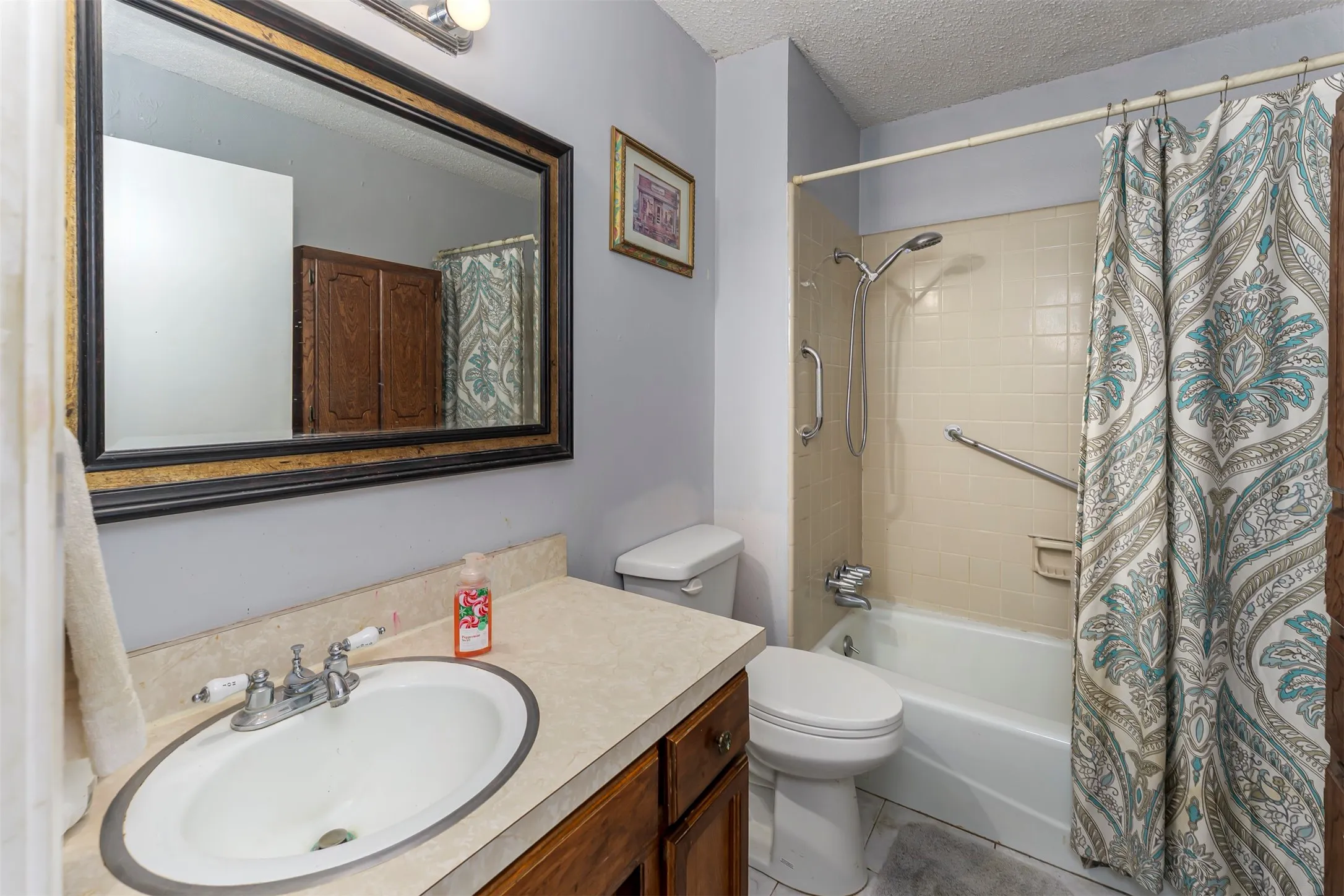 Bathroom featuring a wood vanity with a neutral countertop, an undermount sink, a framed wall mirror, and a tub-shower combination with ceramic tile surround