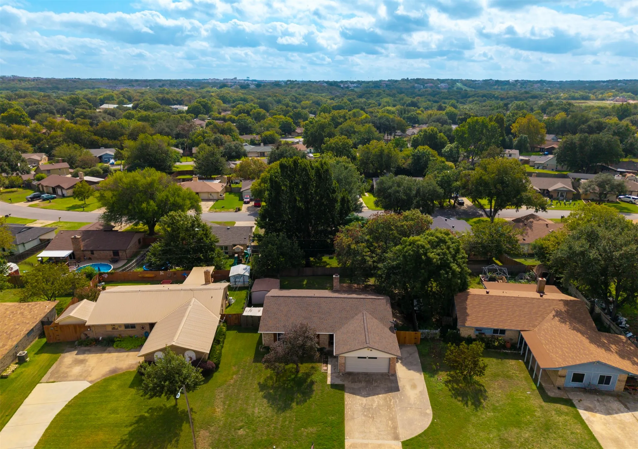 Aerial perspective featuring residential lots with mature canopy trees, paved driveways, and expansive turf lawns