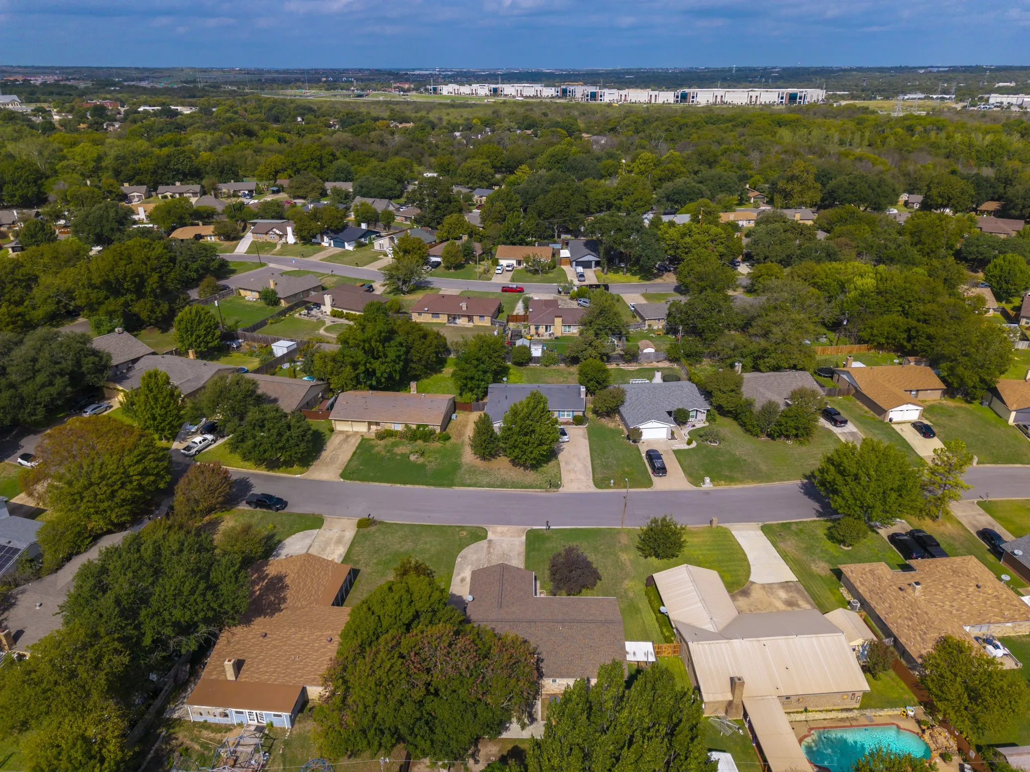Aerial perspective of a suburban neighborhood featuring mature canopy trees, paved street infrastructure, and established landscaping