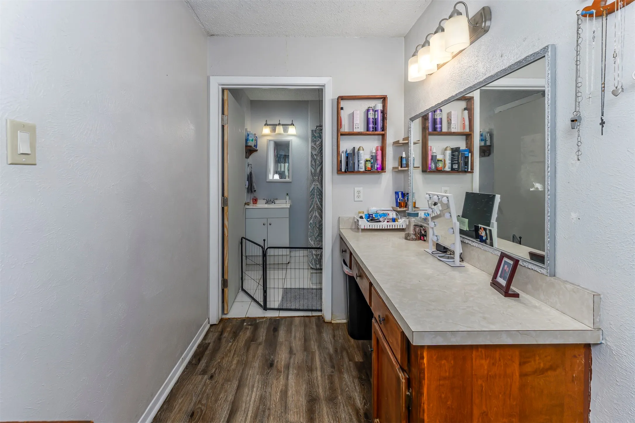 Bathroom featuring wood-finish flooring, a long built-in vanity with a stone-composite countertop, a large wall-mounted vanity mirror, and multi-bulb overhead lighting