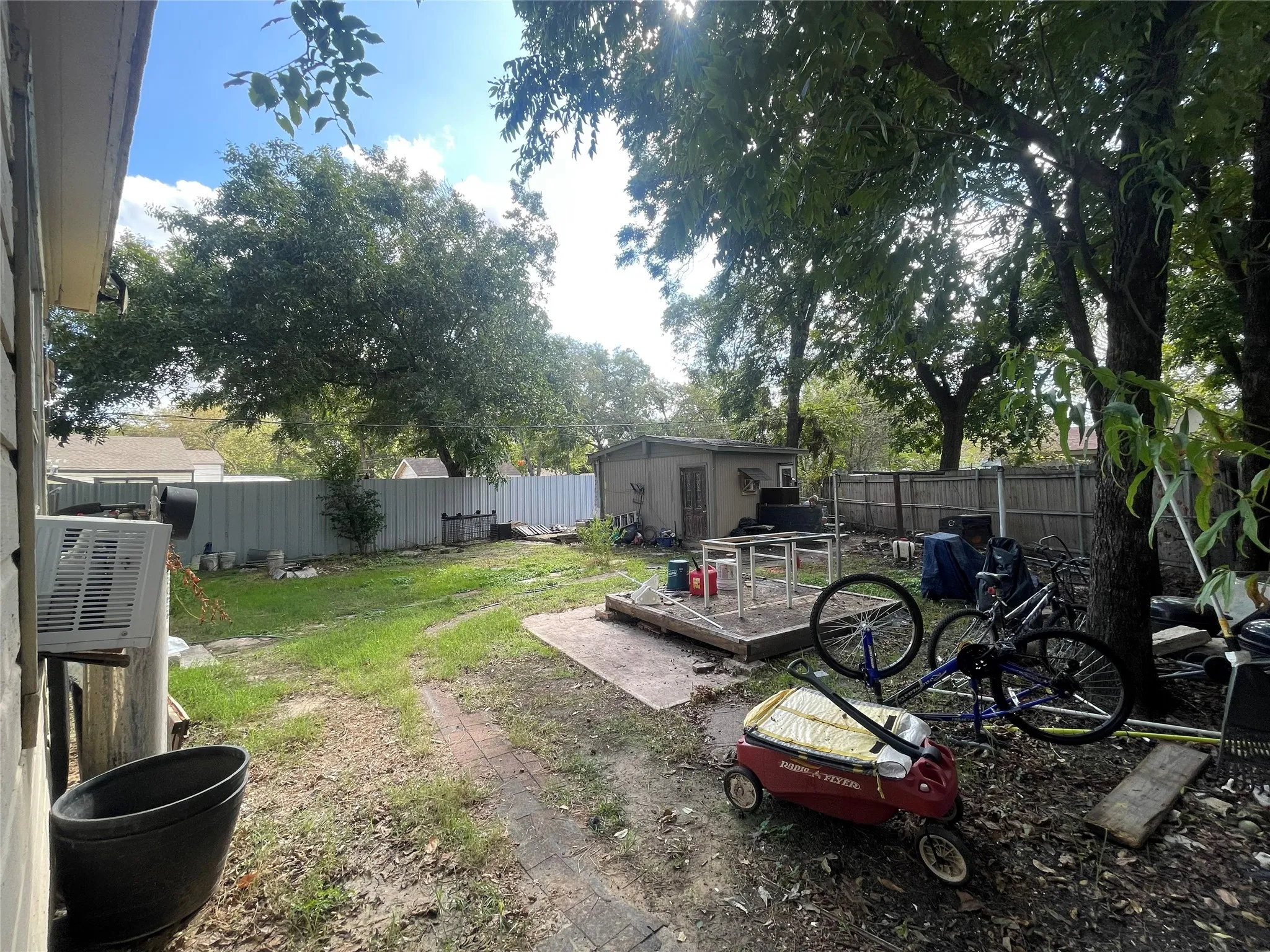 Backyard featuring mature trees, a detached storage structure, and a brick-paved pathway enclosed by perimeter fencing
