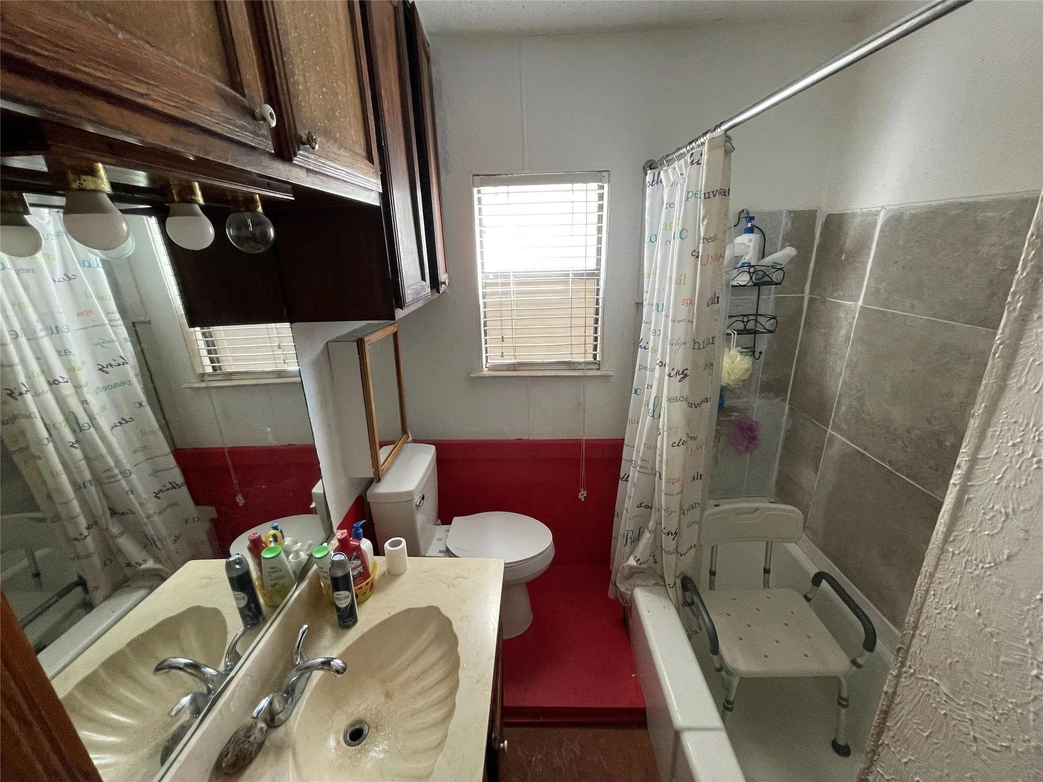 Bathroom featuring a molded shell-design sink, wood-finish cabinetry, a large wall-mounted mirror, and tile-surround bathtub