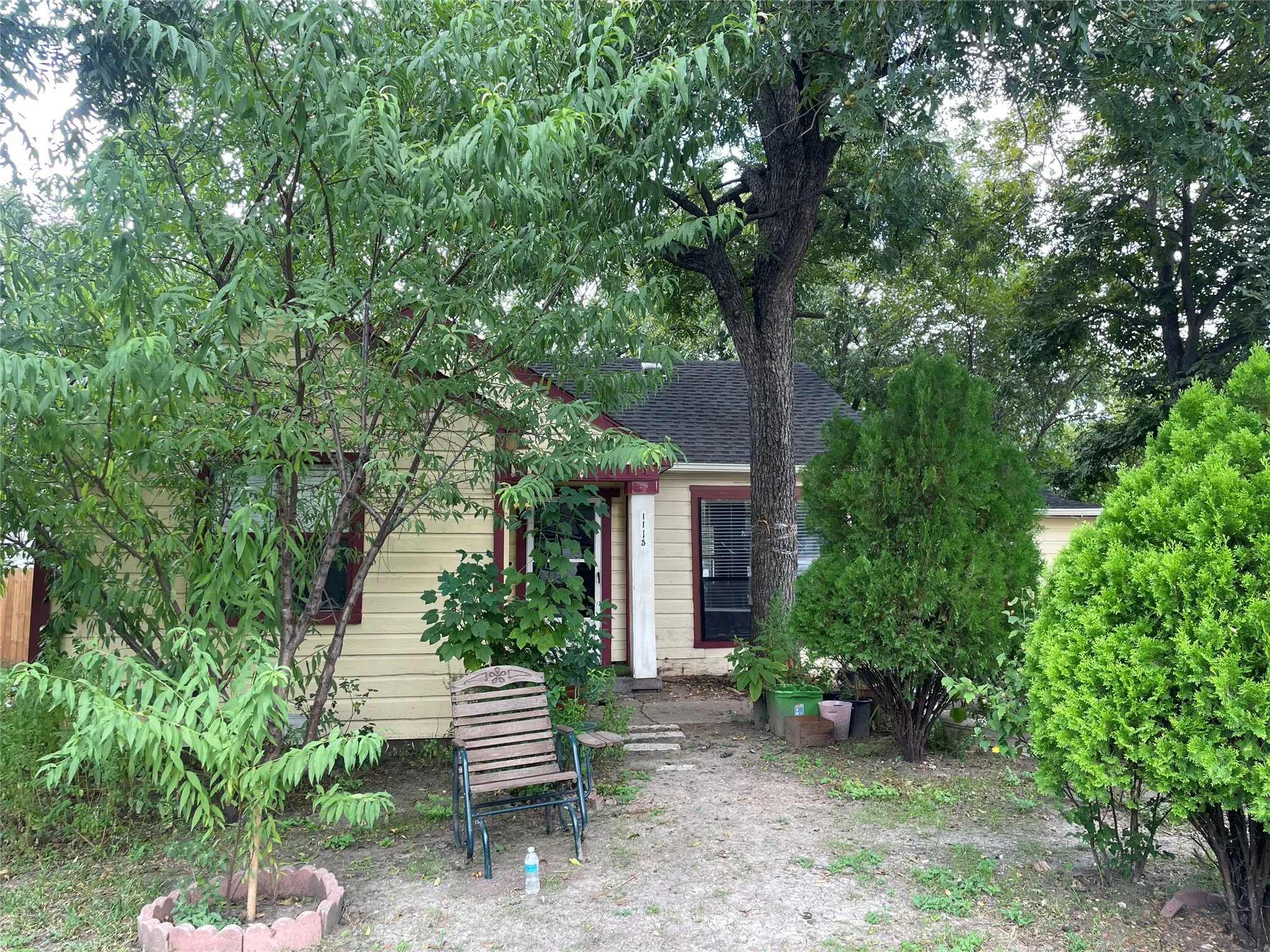 Single-story exterior featuring horizontal siding, dark-toned roof shingles, and mature trees