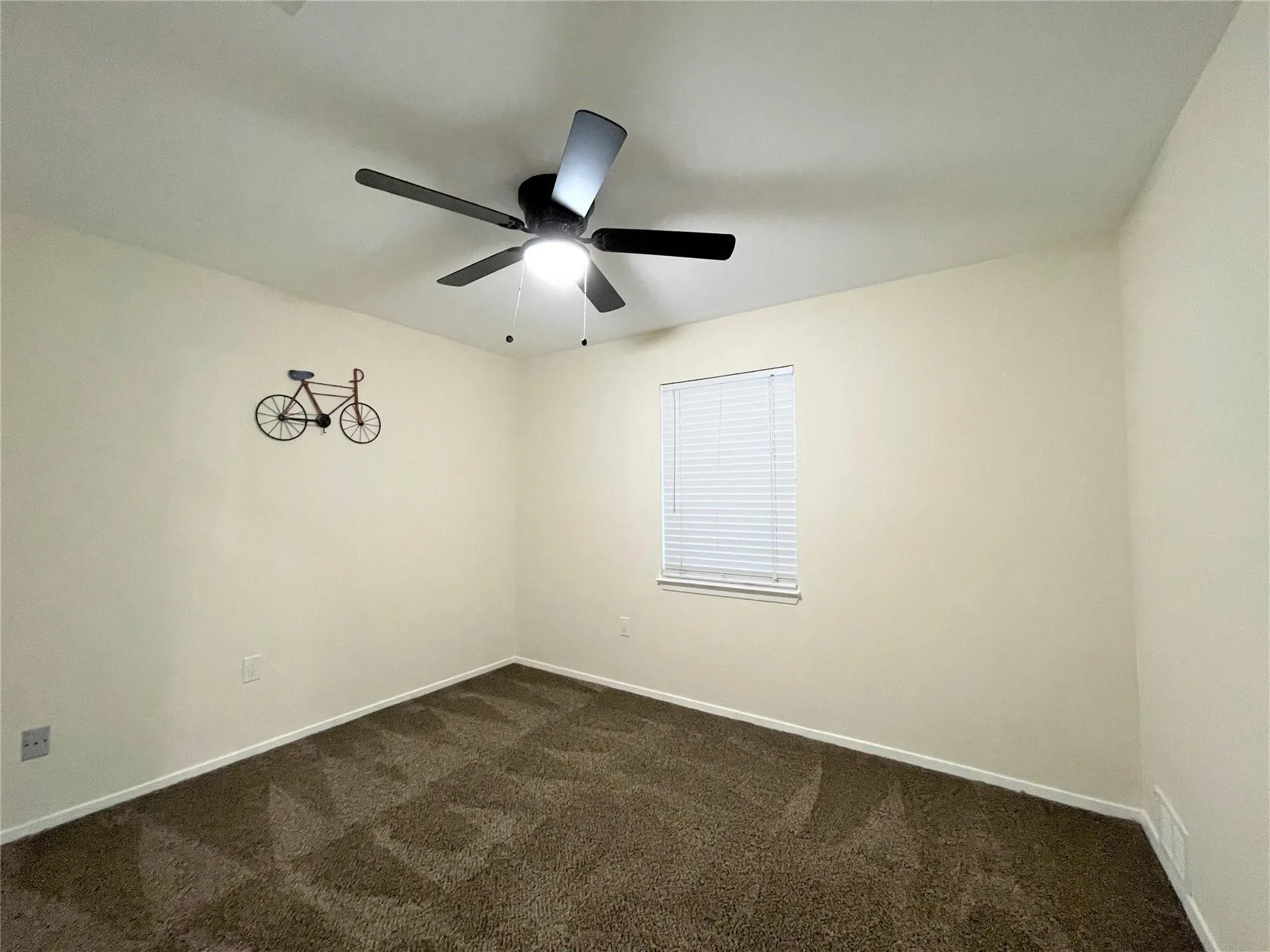 Neutral-toned room featuring wall-to-wall carpeting, a multi-blade ceiling fan with an integrated light fixture, and a window with horizontal blinds