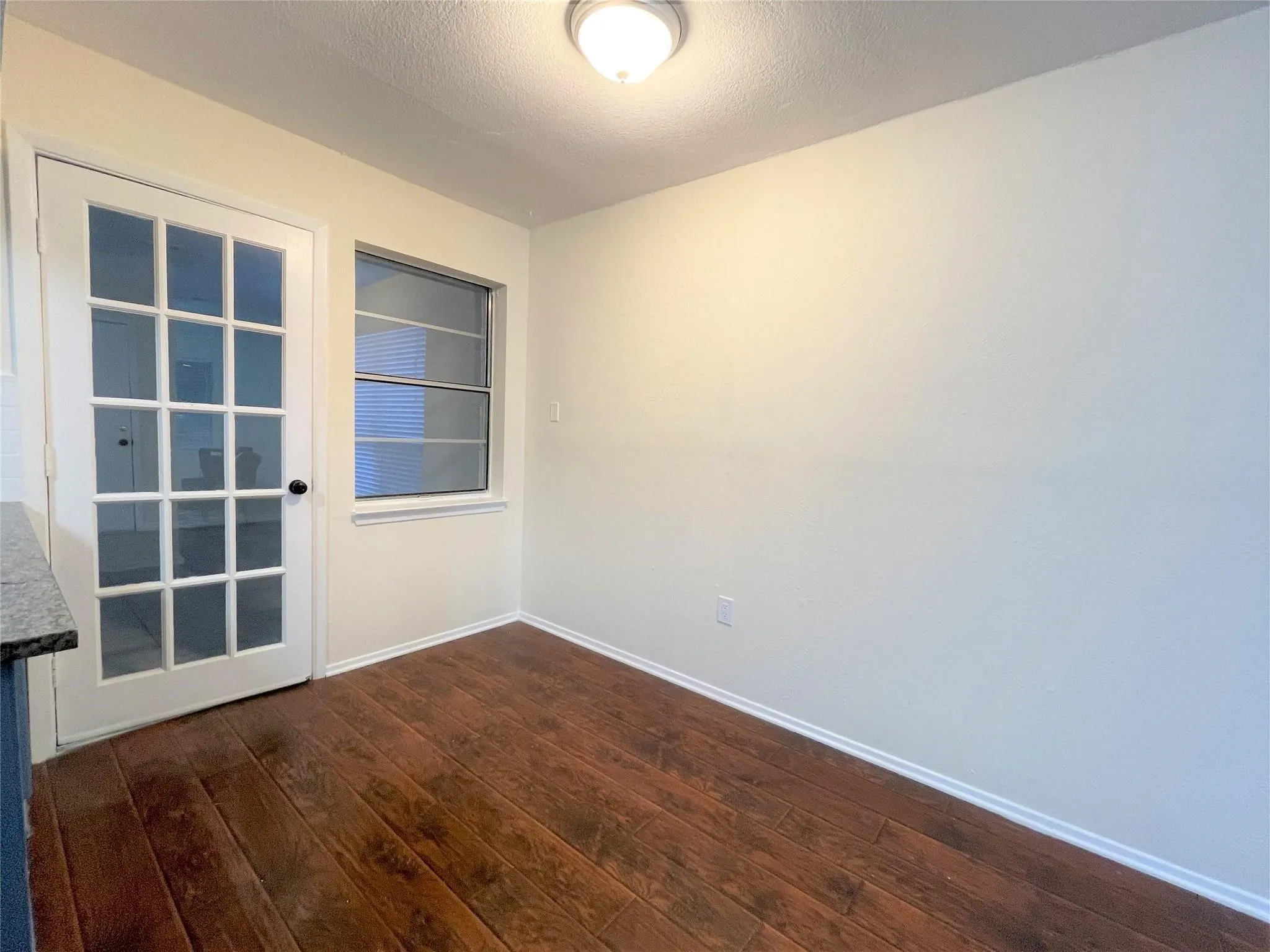 Wood-finish flooring, multi-pane glass door, single-hung window, and a flush-mount ceiling light fixture
