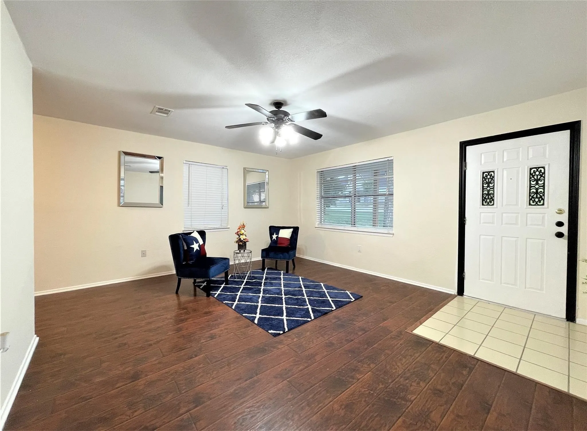 Living area featuring wood-finish flooring, neutral wall paint, a ceiling fan with integrated lighting, and a multi-panel door with decorative inserts