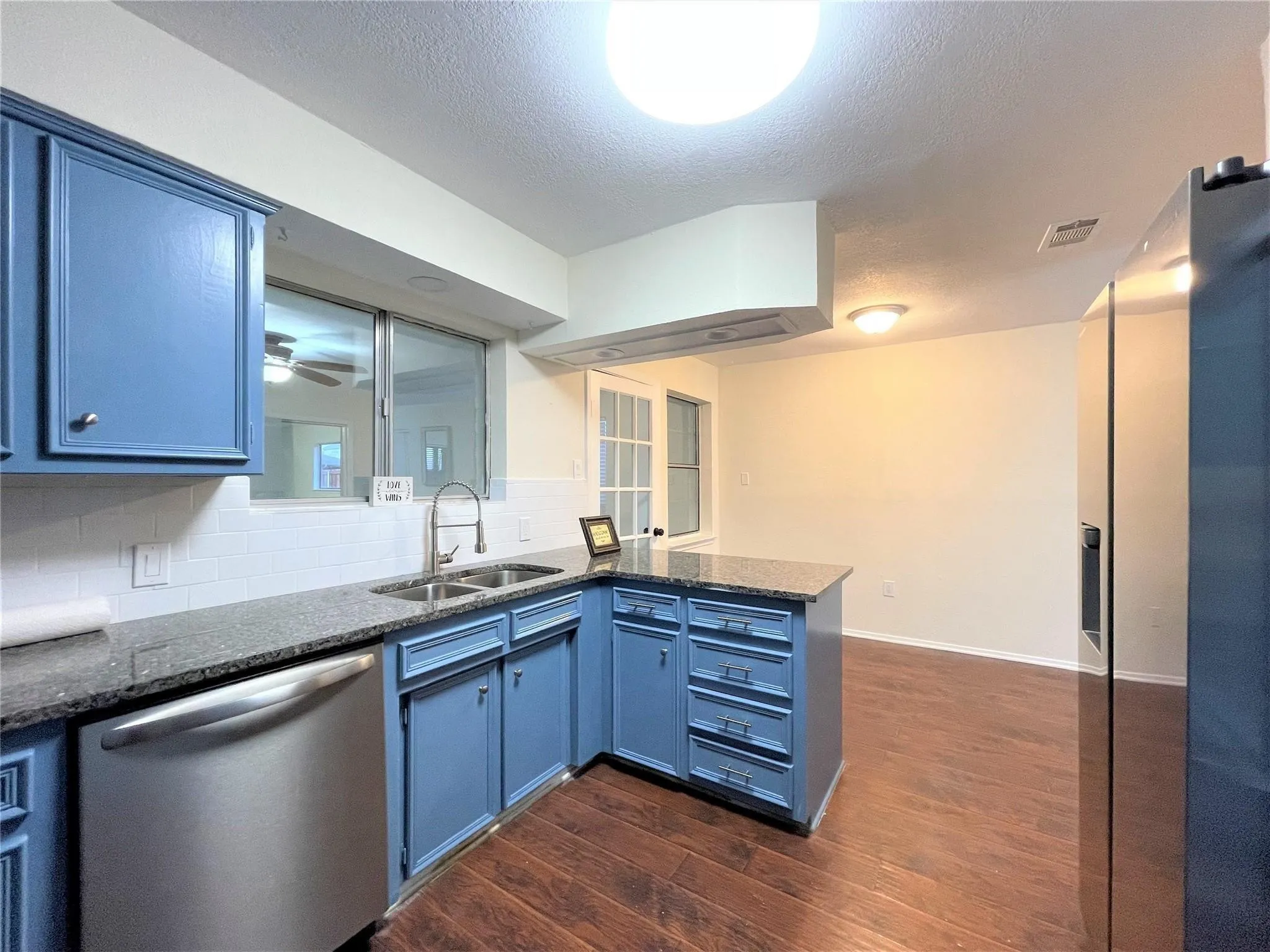 Kitchen featuring blue cabinetry, stone-finish countertops, subway tile backsplash, stainless steel dishwasher, and wood-finish flooring