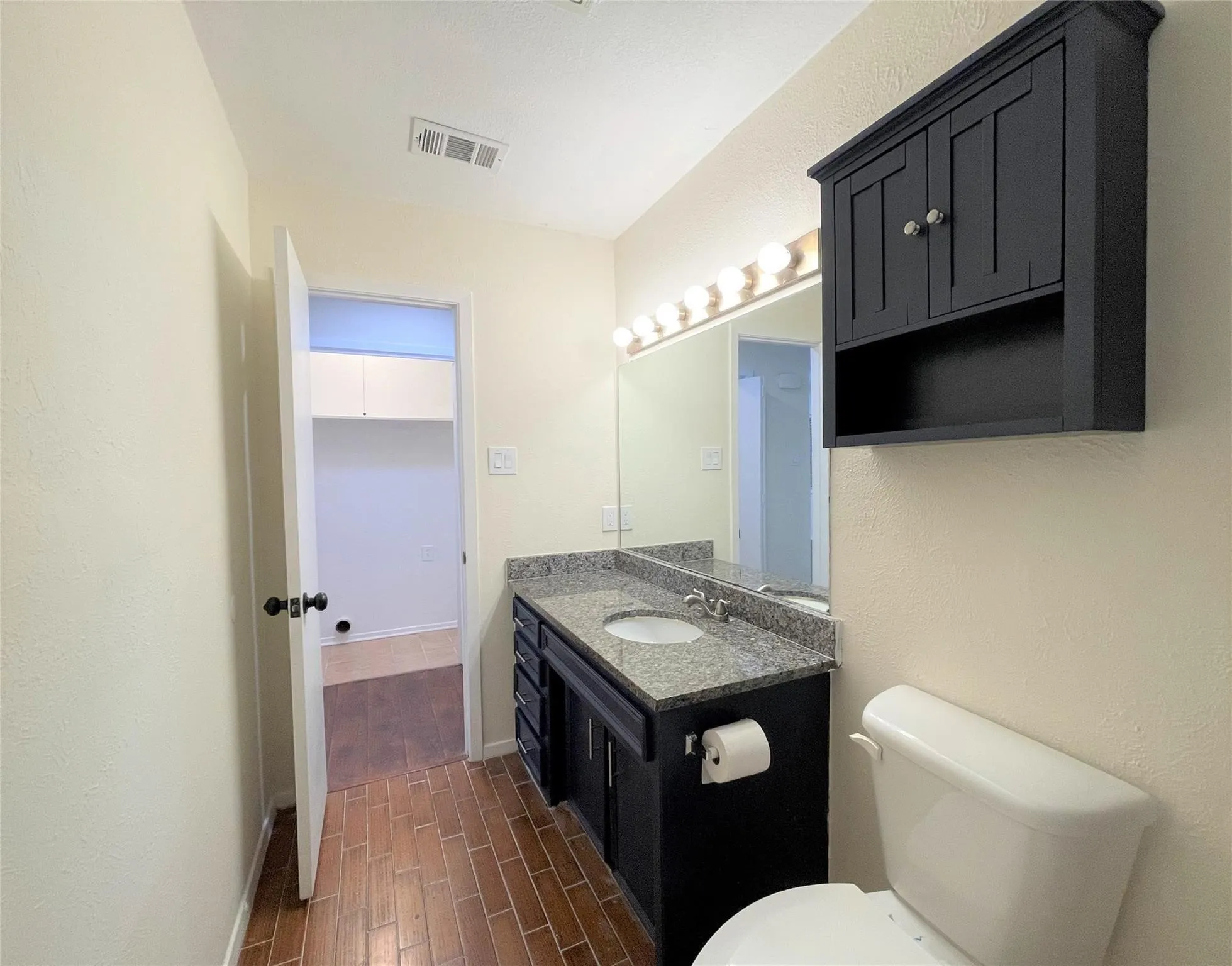 Bathroom featuring a stone-topped vanity with dark cabinetry, a wall-mounted medicine cabinet, a full-width vanity mirror with multi-bulb lighting, and tile flooring