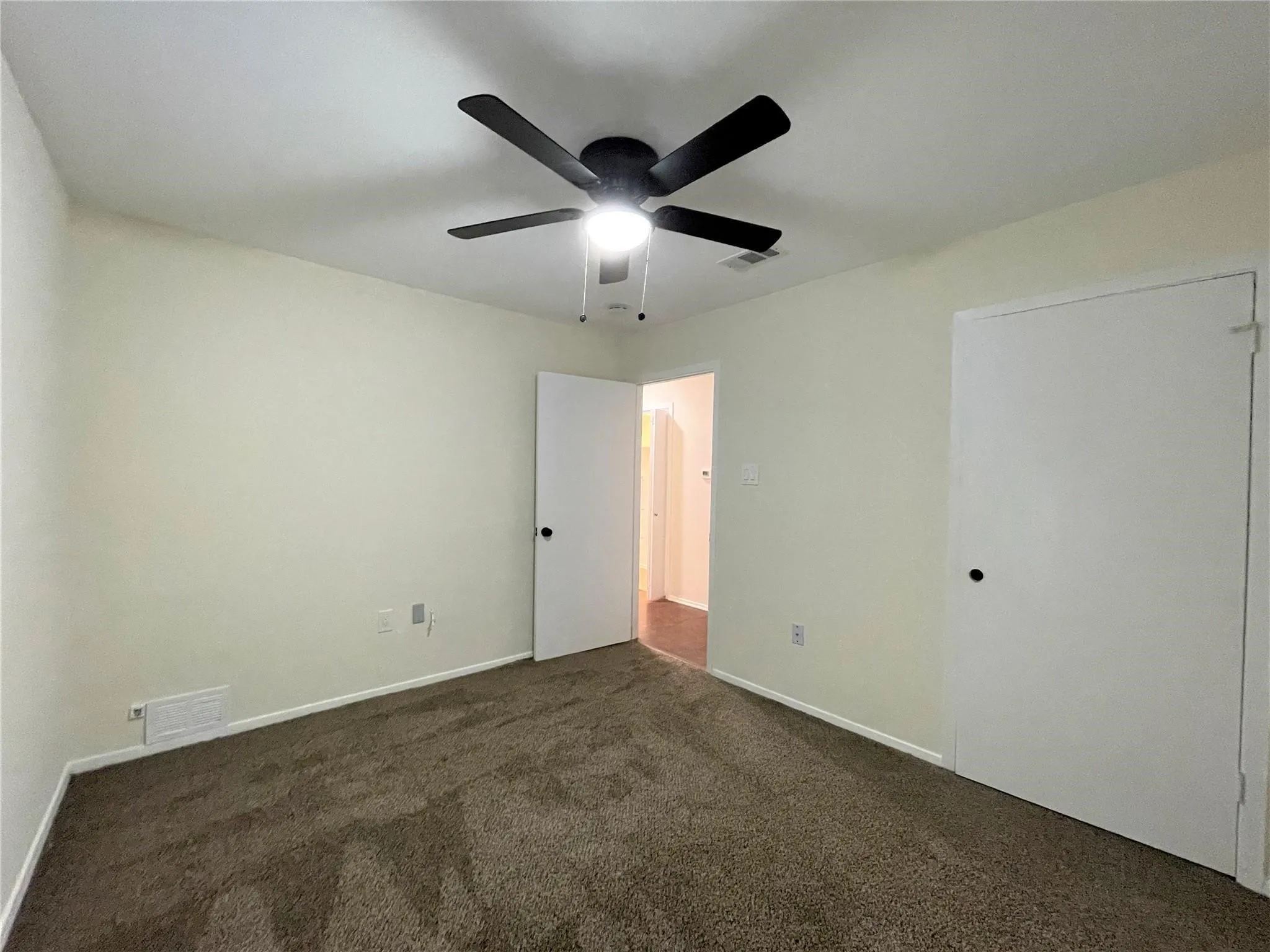 Neutral wall finish with carpeting and a matte black ceiling fan featuring an integrated light fixture, complemented by white interior doors