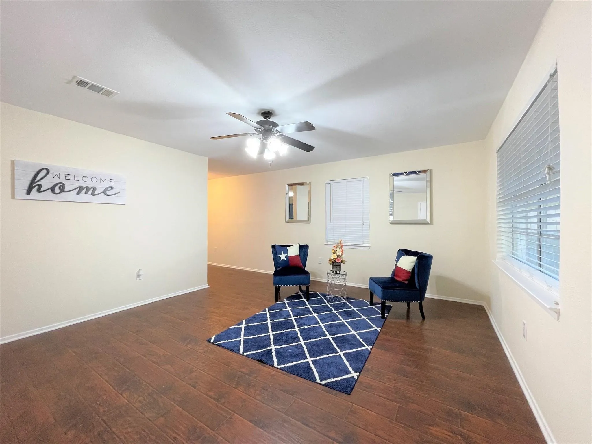 Living space featuring wood-finish flooring, a multi-blade ceiling fan with integrated lighting, and horizontal window blinds