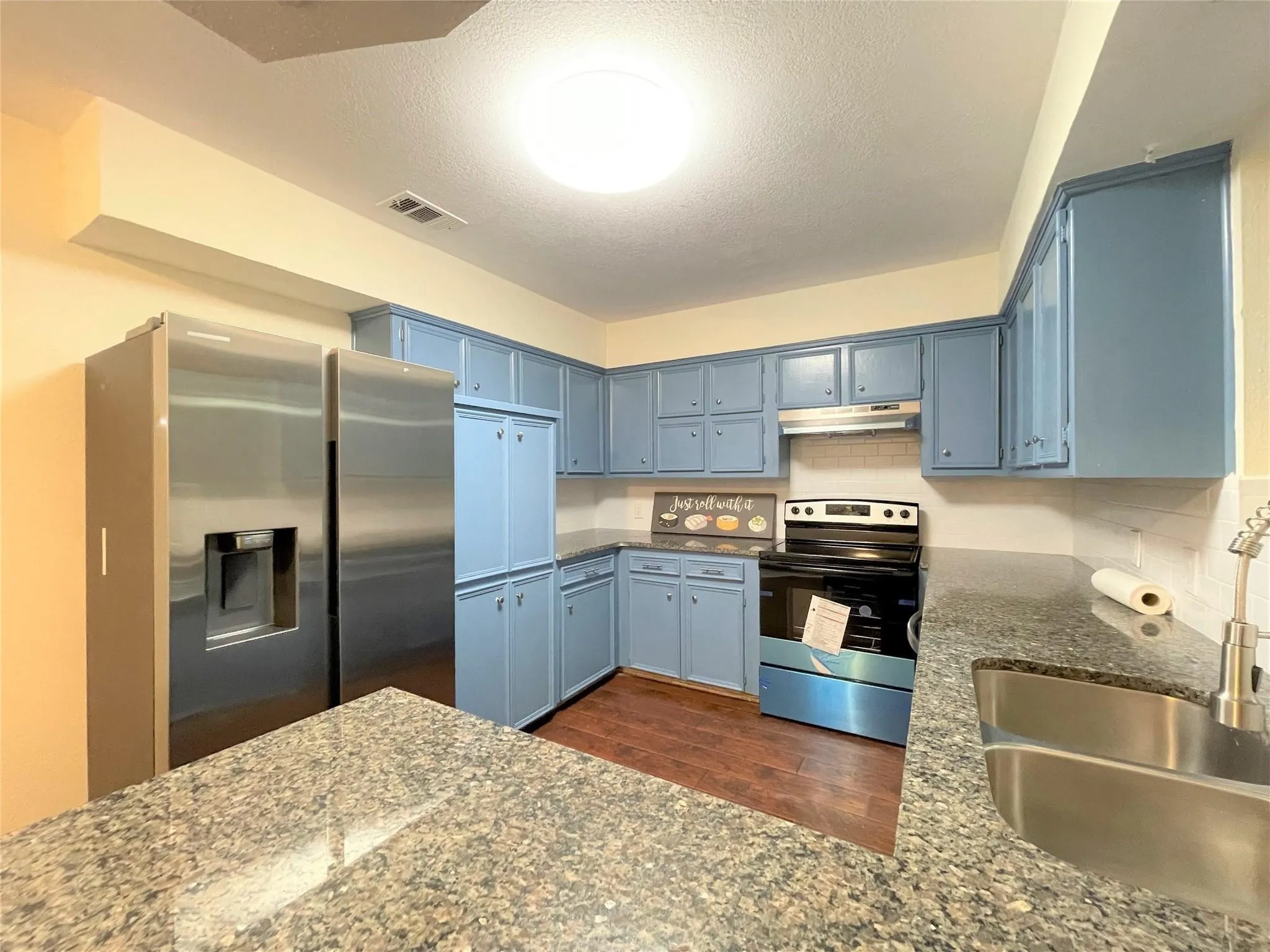 Kitchen featuring blue cabinetry, stone-finish countertops, stainless steel appliances, a double-basin undermount sink with a pull-down sprayer, and wood-finish flooring