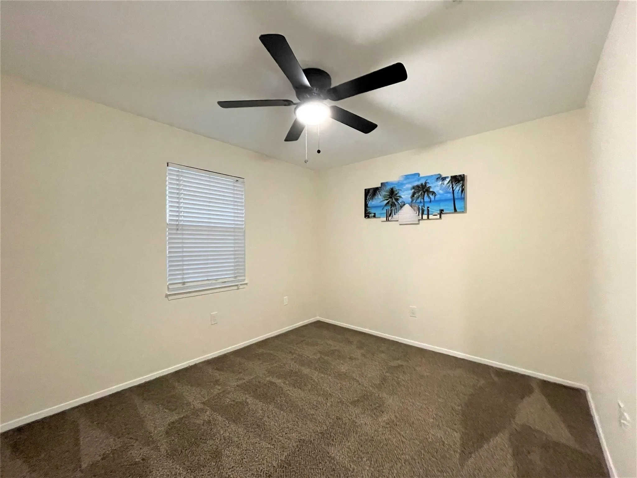 Neutral interior space featuring carpeted flooring, a ceiling fan with integrated lighting, and a window equipped with horizontal blinds