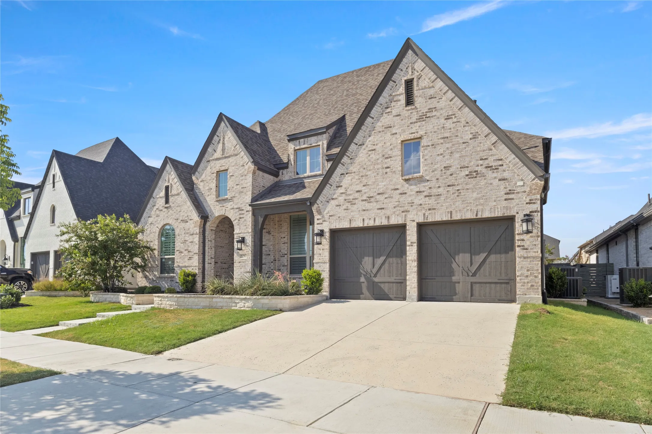 Two-story brick exterior featuring a steeply pitched roofline, decorative gable accents, and a two-car garage with carriage-style doors