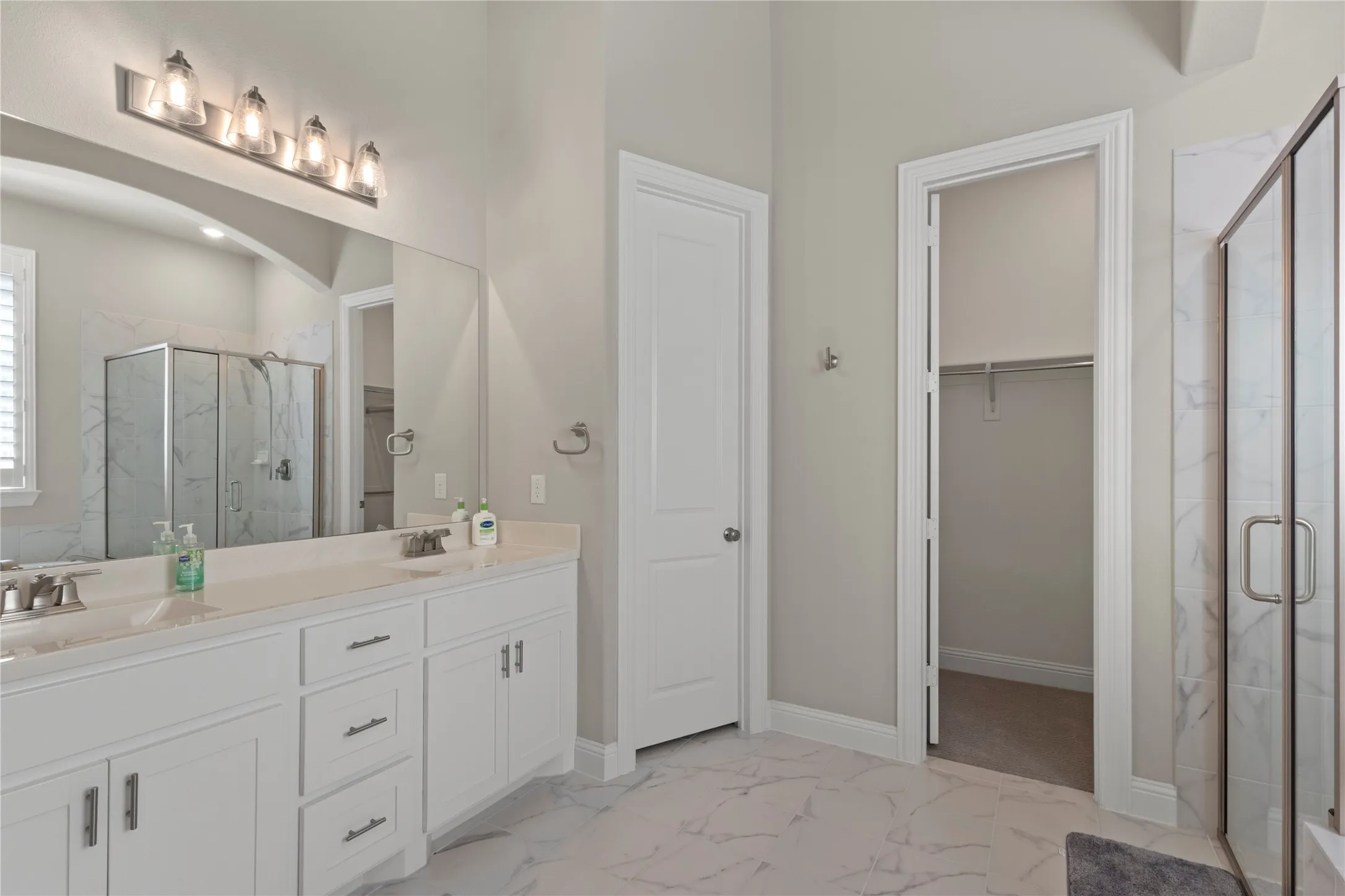 Double vanity featuring white cabinetry, a neutral solid-surface countertop, full-width mirror, five-light fixture, and walk-in shower with stone-patterned tile surround