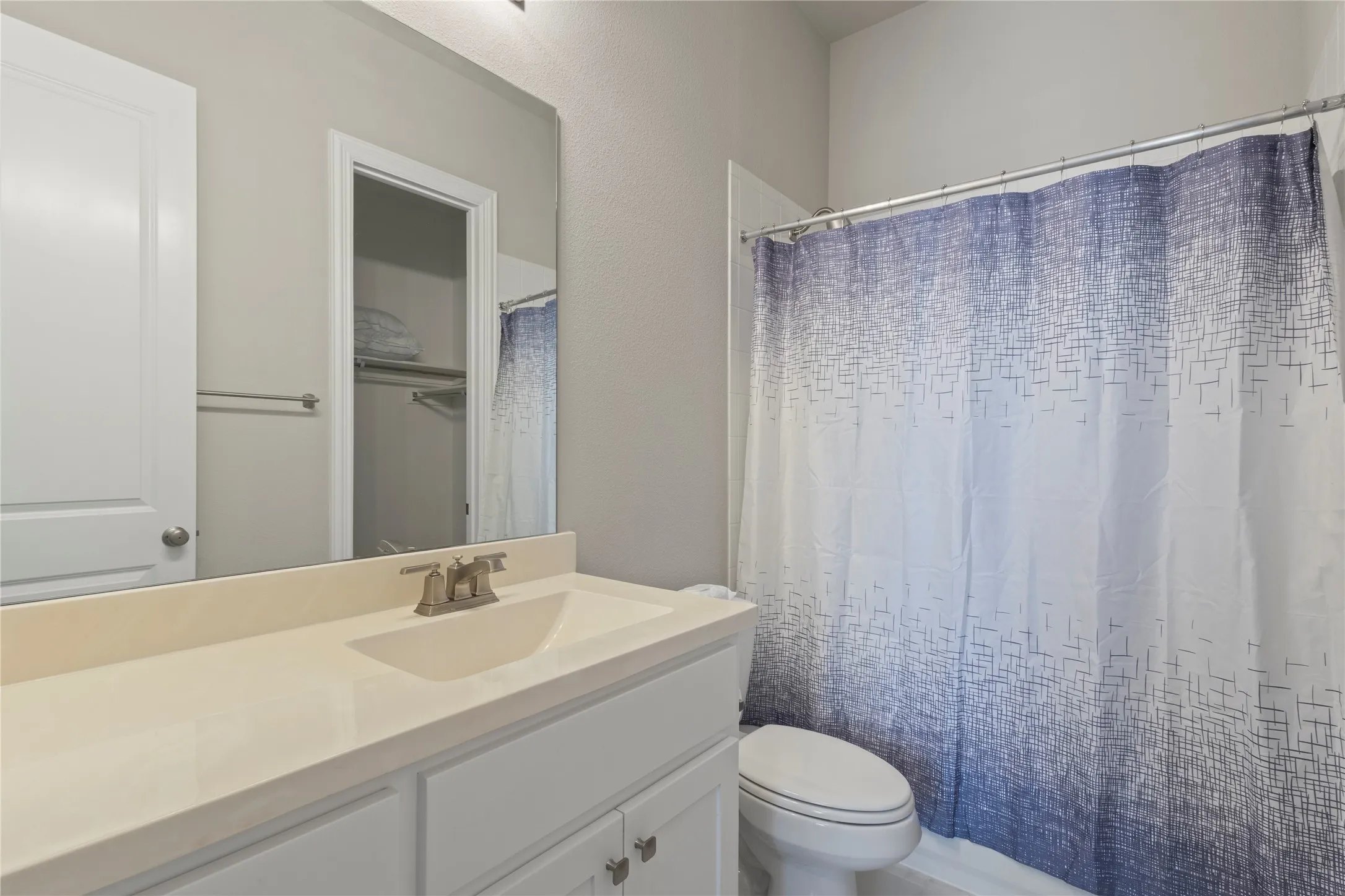 Bathroom vanity with a solid-surface countertop and integrated sink, chrome faucet, large wall-mounted mirror, and a tub-shower combination with a metal curtain rod
