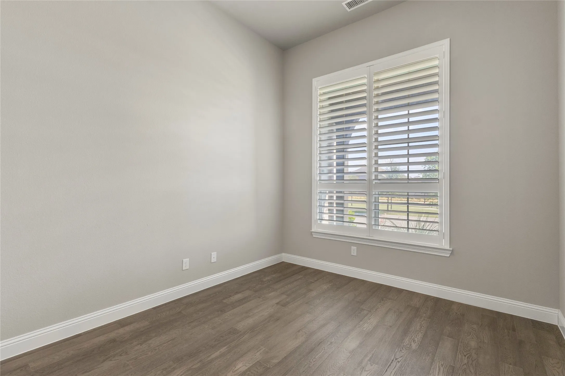 Neutral-toned interior featuring high ceilings, wood-finish flooring, and a large window with white plantation shutters