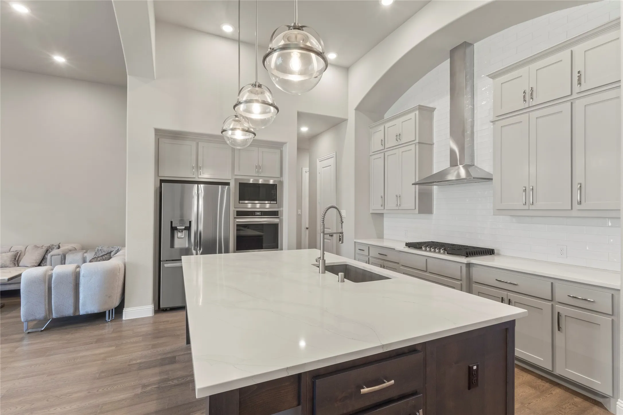 Kitchen featuring a quartz-topped center island with a stainless steel undermount sink, custom cabinetry, stainless steel appliances, and a tiled backsplash