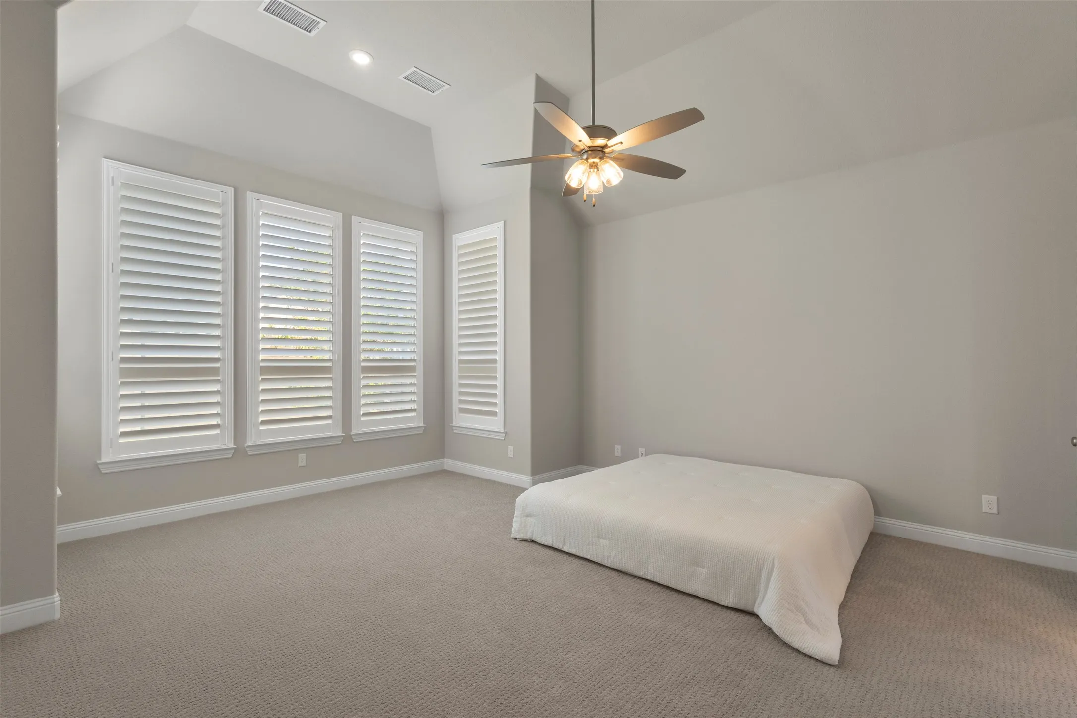 Vaulted ceilings, carpeted flooring, white plantation shutters, and a multi-light ceiling fan