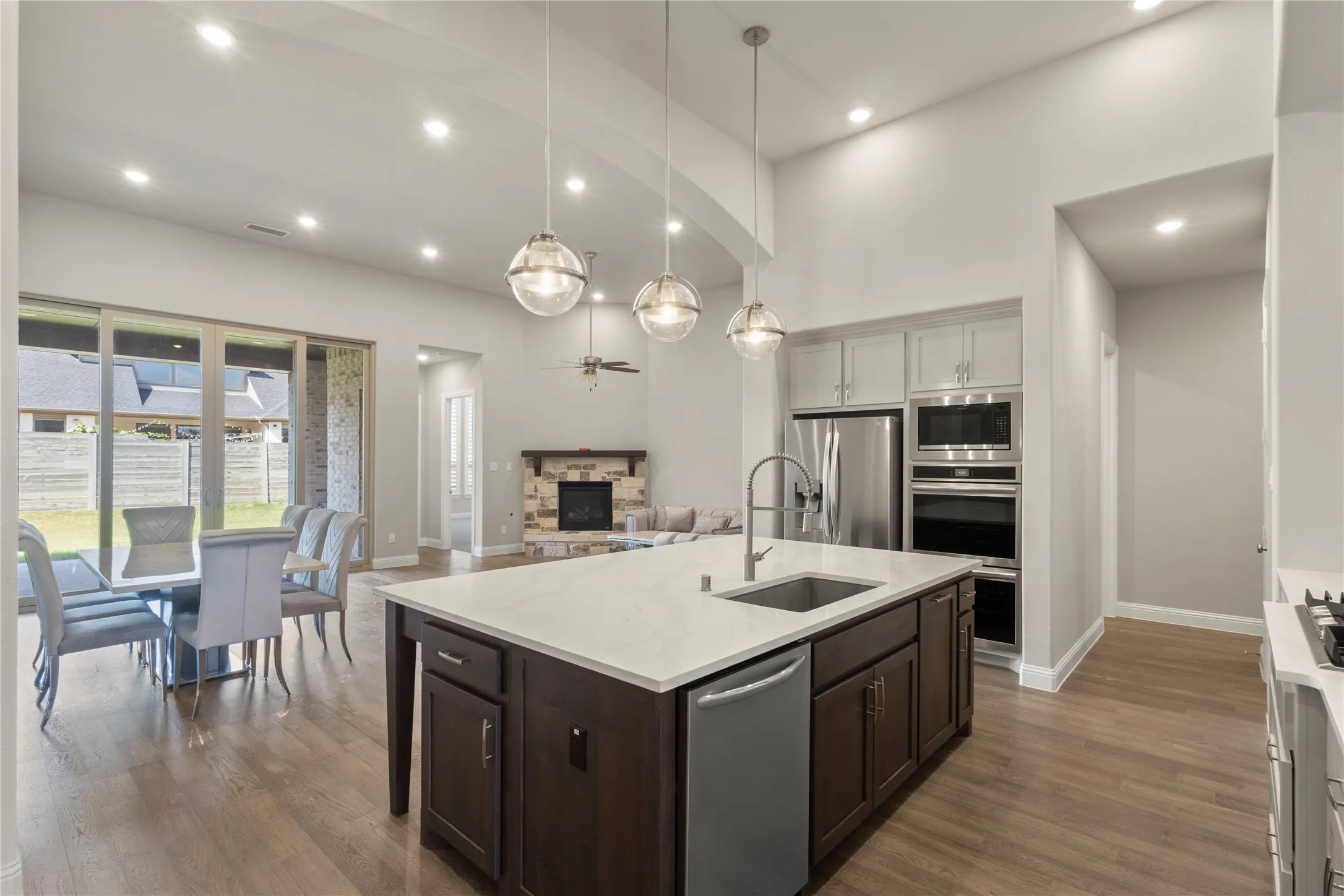 Open-concept kitchen featuring an island with a stone-finish countertop, stainless steel appliances, and wood-finish flooring