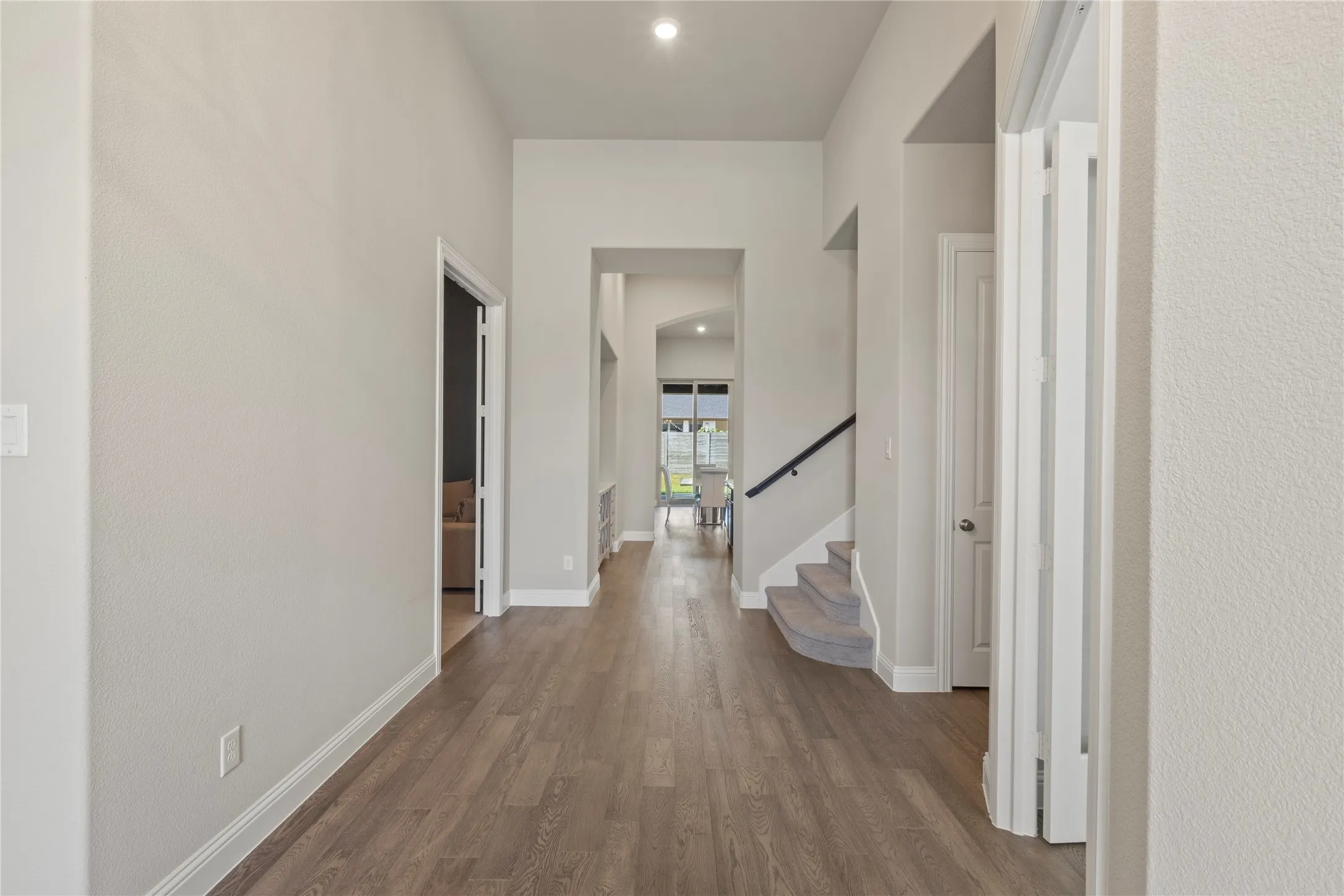 High-ceilinged entry featuring wood-finish flooring, recessed lighting, and a staircase with a dark metal handrail