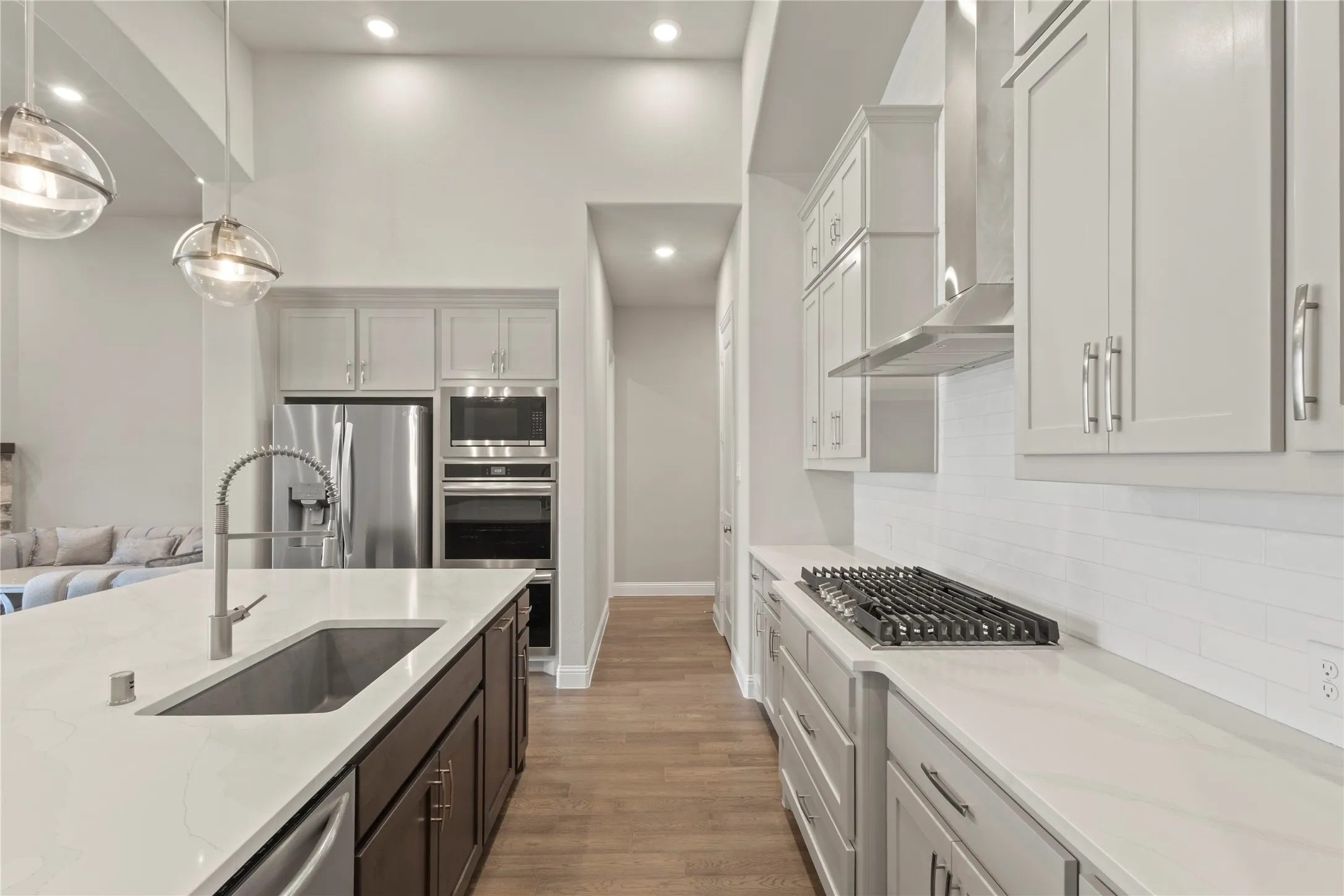 Kitchen featuring a spacious island with a single-basin undermount sink, quartz countertops, light-toned cabinetry, stainless steel built-in appliances, and wood-finish flooring