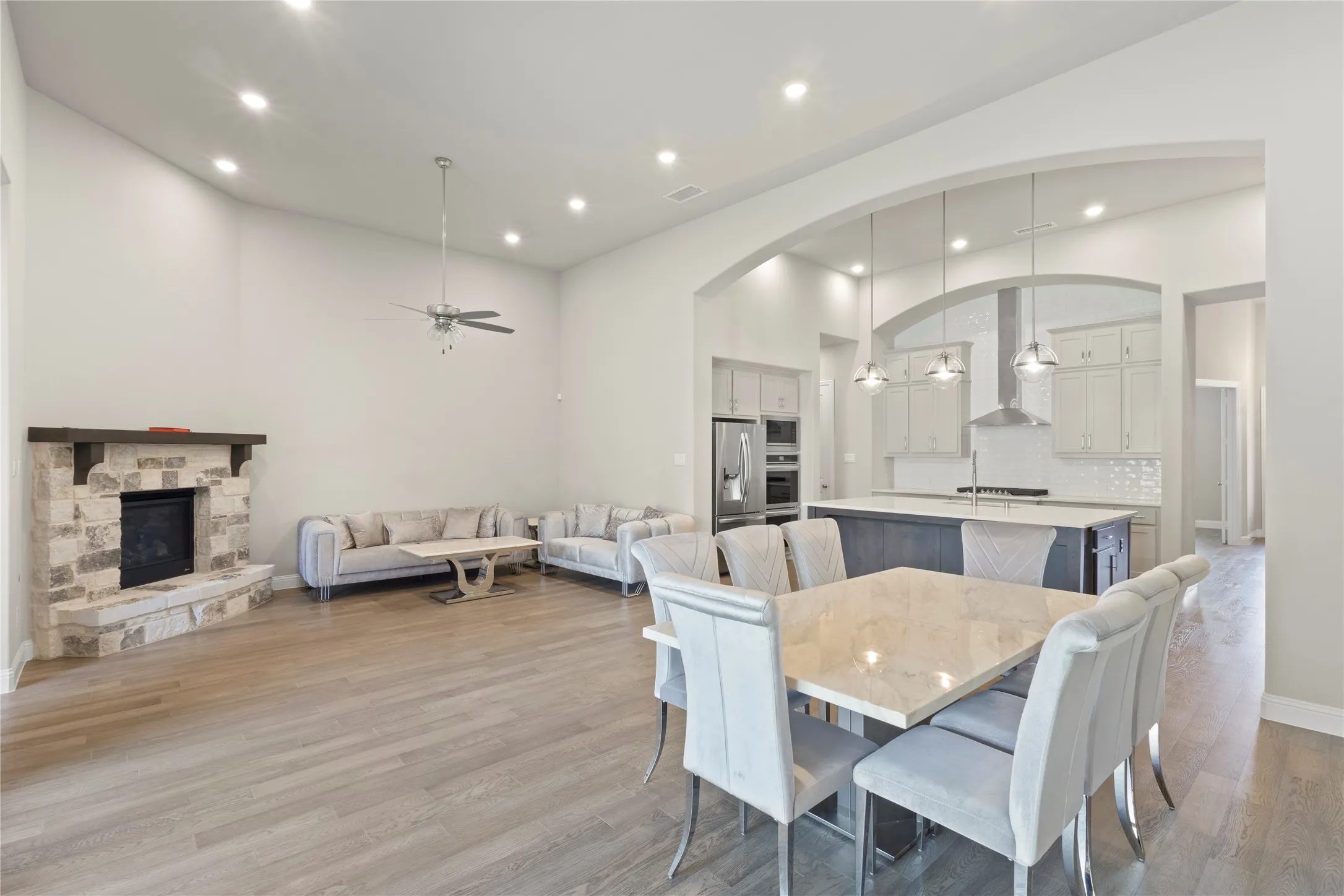 Open-concept interior featuring wood-finish flooring, a stone fireplace with a timber mantel, vaulted ceilings, a central kitchen island, and recessed lighting