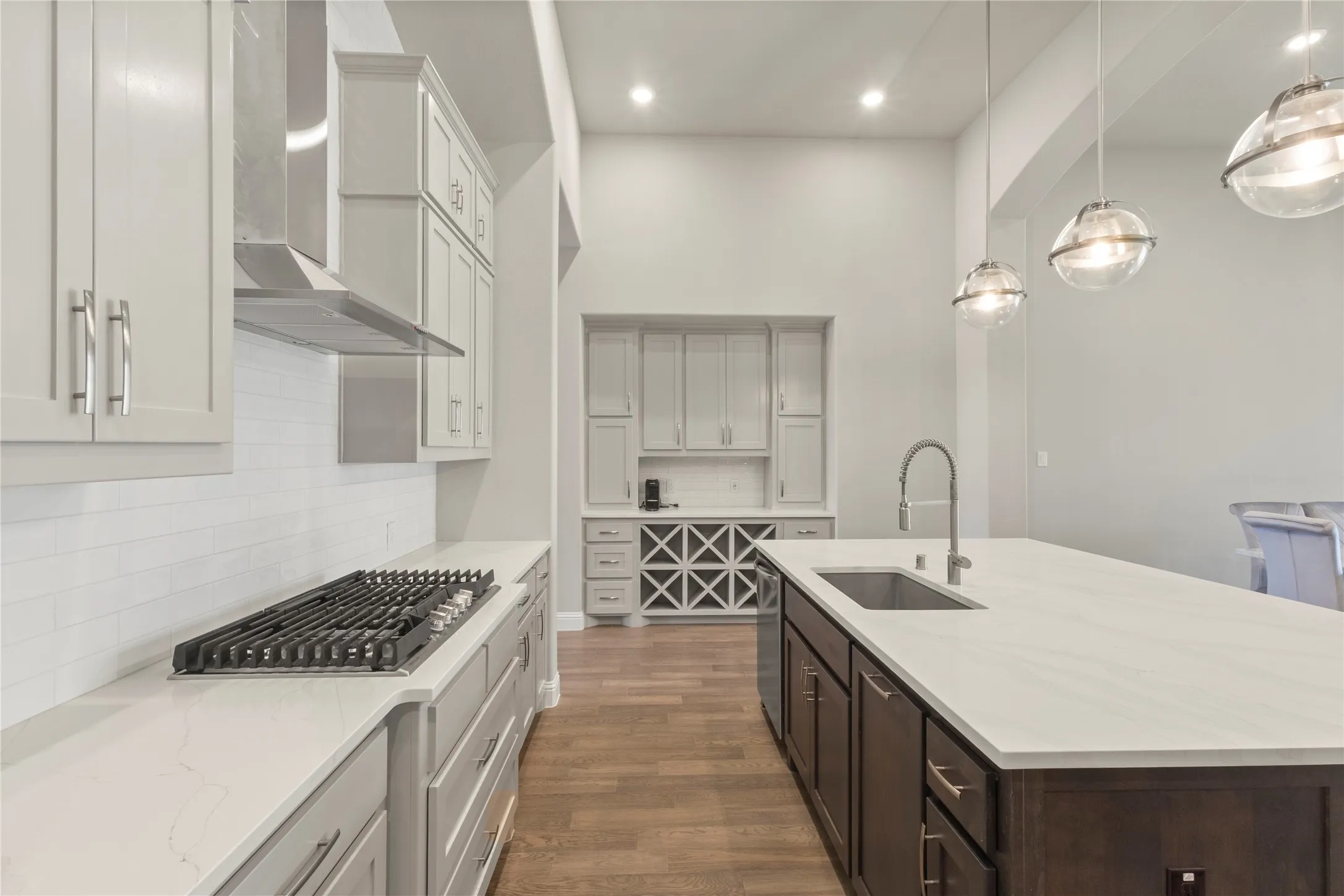 Kitchen featuring a large central island with quartz countertops, custom cabinetry, built-in wine storage, stainless steel gas cooktop, and glass pendant lighting