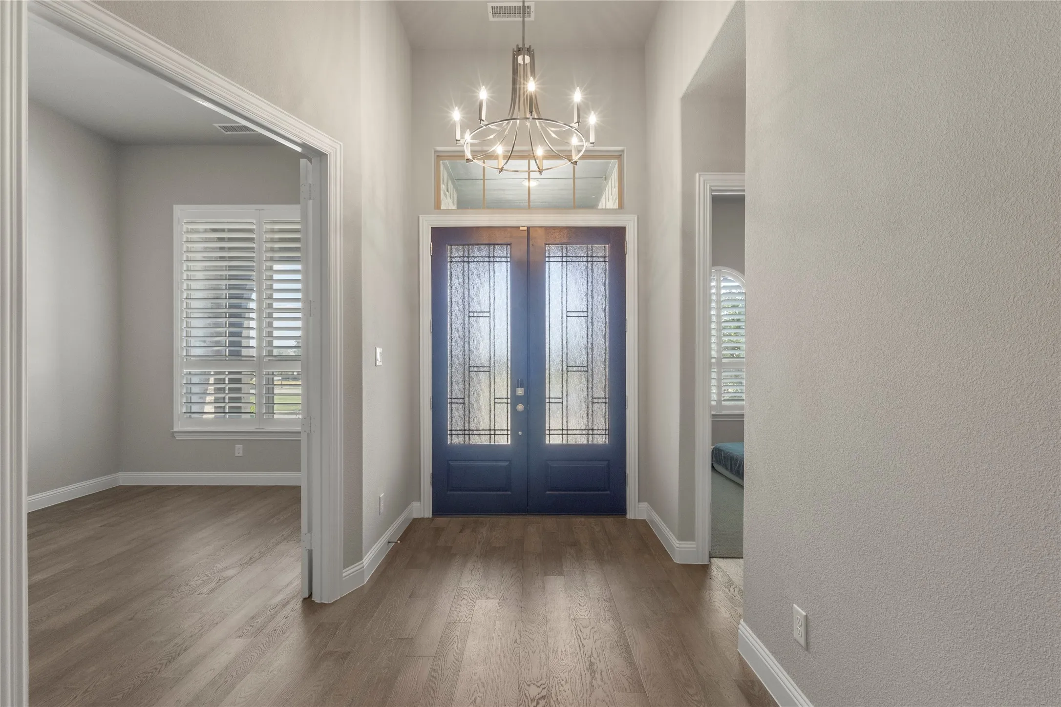 Foyer featuring double entry doors with decorative glass inserts, a transom window, wood-finish flooring, and a multi-arm chandelier