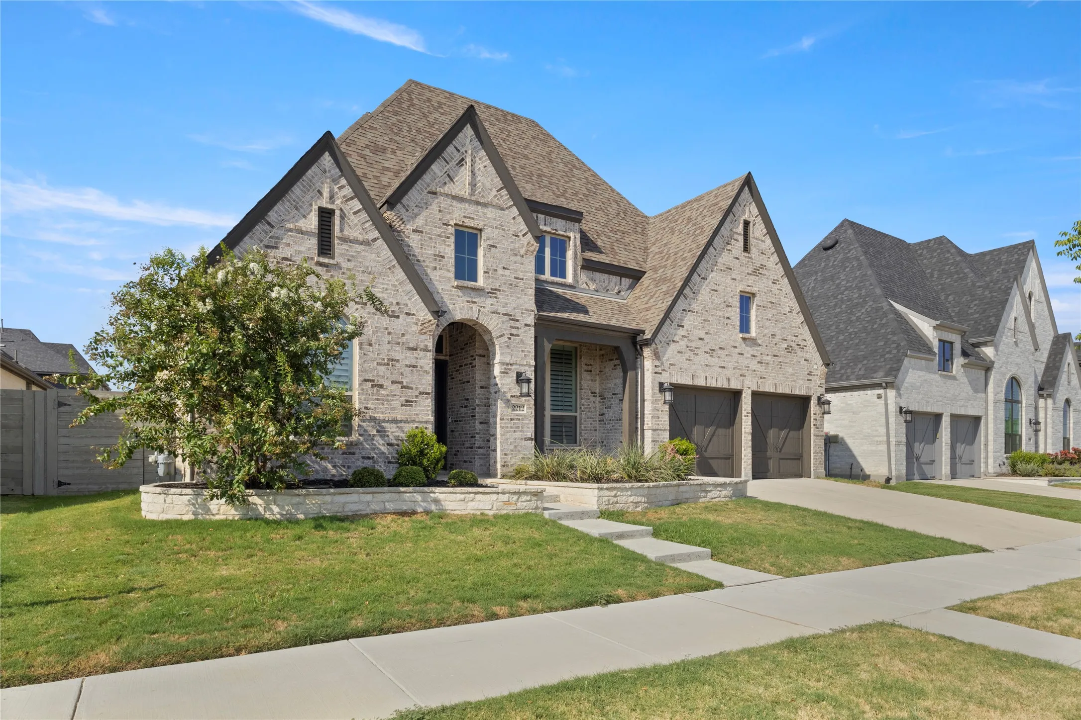 Brick exterior with gabled roofline, arched entryway, multi-car garage, and stone-bordered landscaping