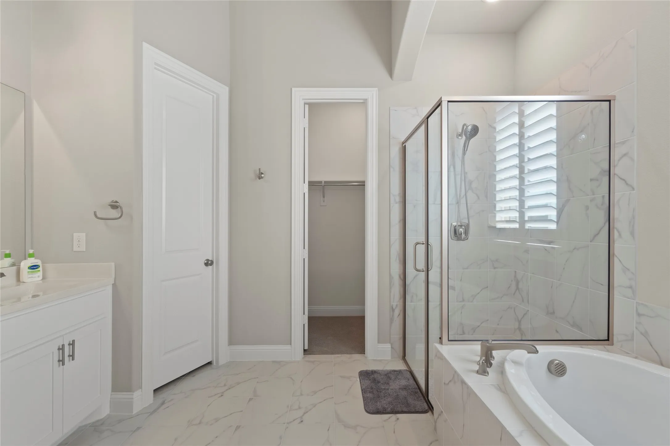 Bathroom featuring a white vanity cabinet, separate soaking tub, glass-enclosed shower with tiled surround, and large-format flooring