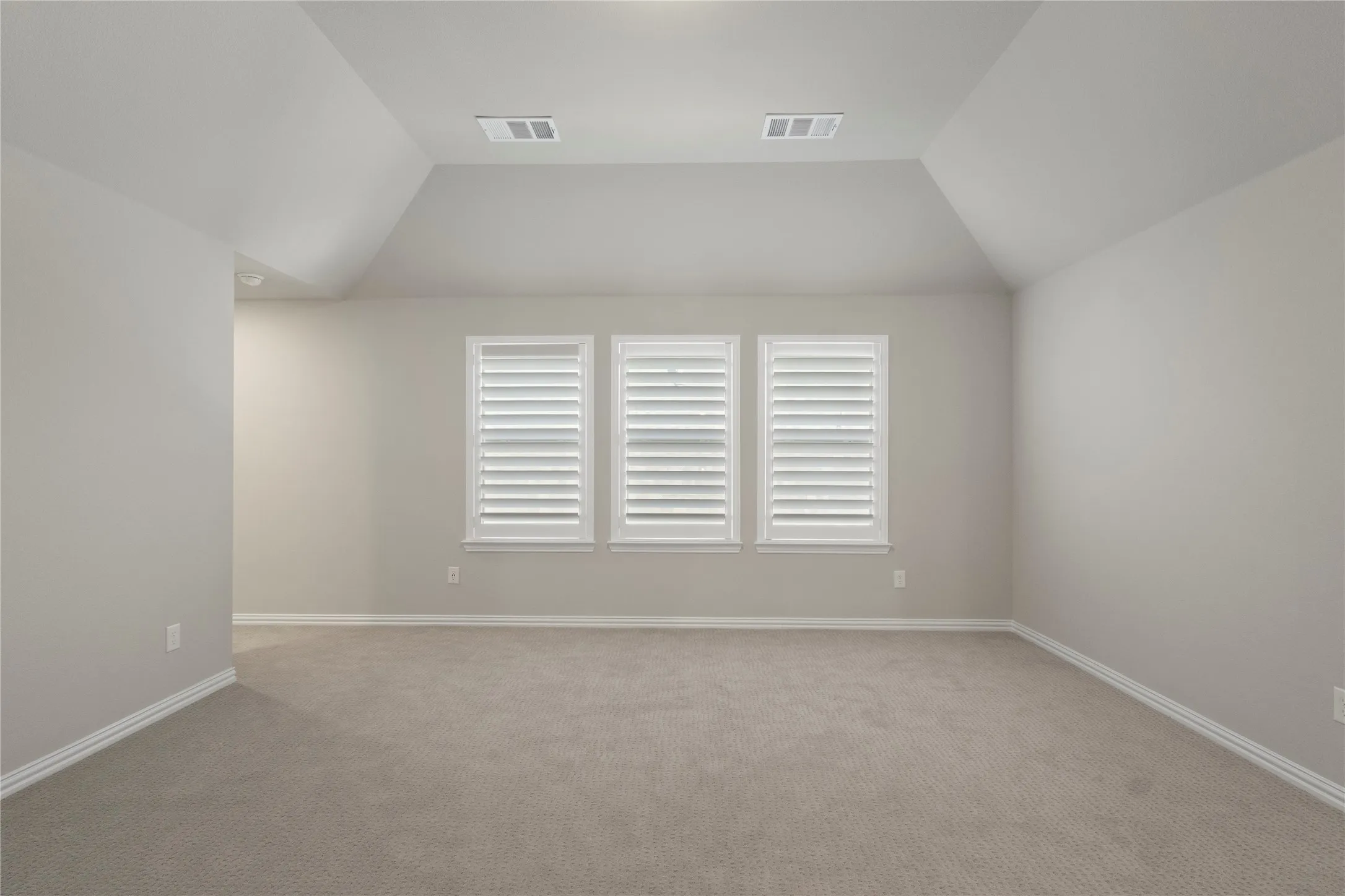 Vaulted ceiling, neutral wall tones, carpeted flooring, and three windows featuring interior shutters