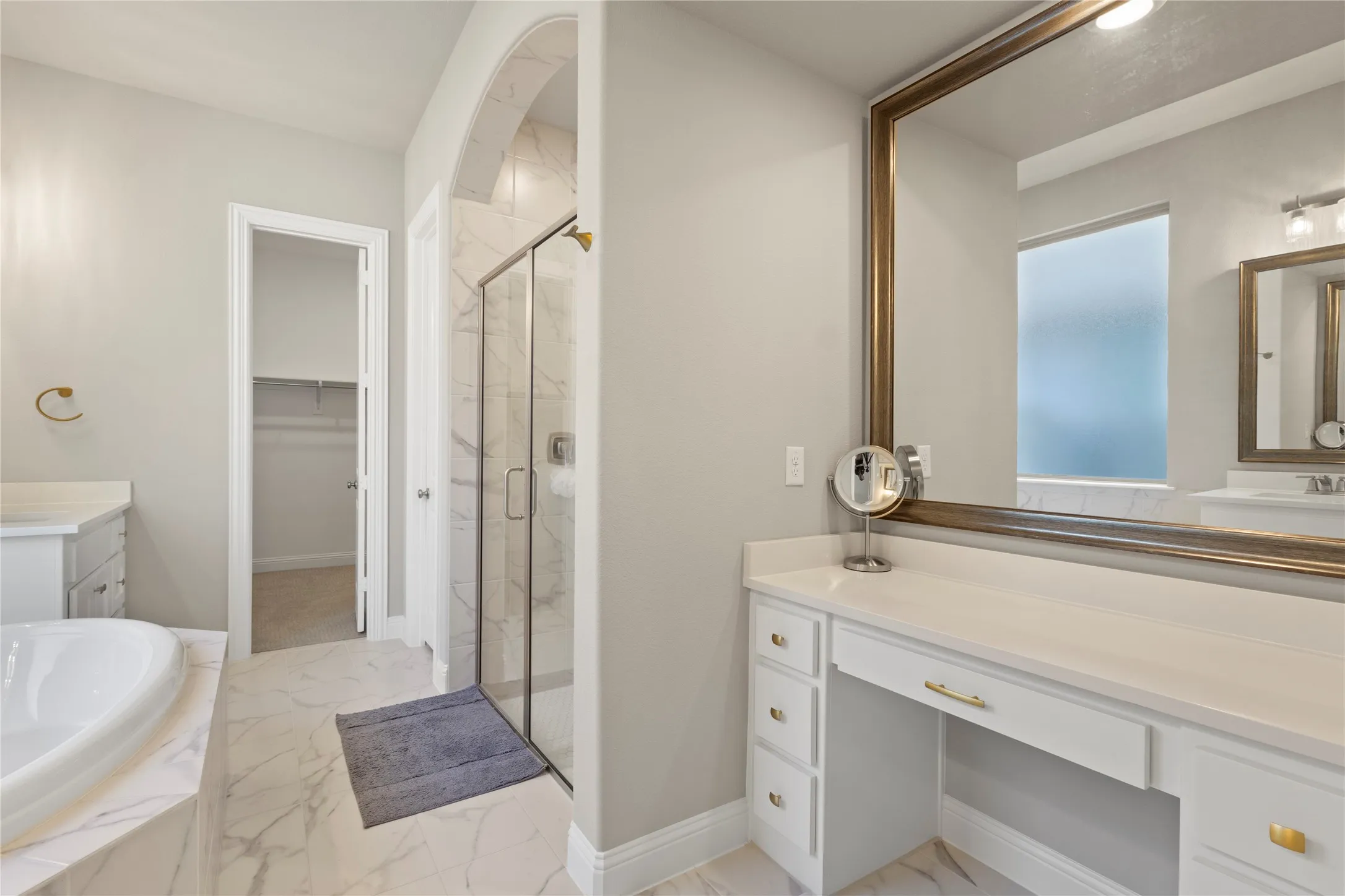 Bathroom featuring a soaking tub with stone-finish surround, walk-in shower with glass enclosure, dual vanity cabinetry with integrated seated station, and tile flooring