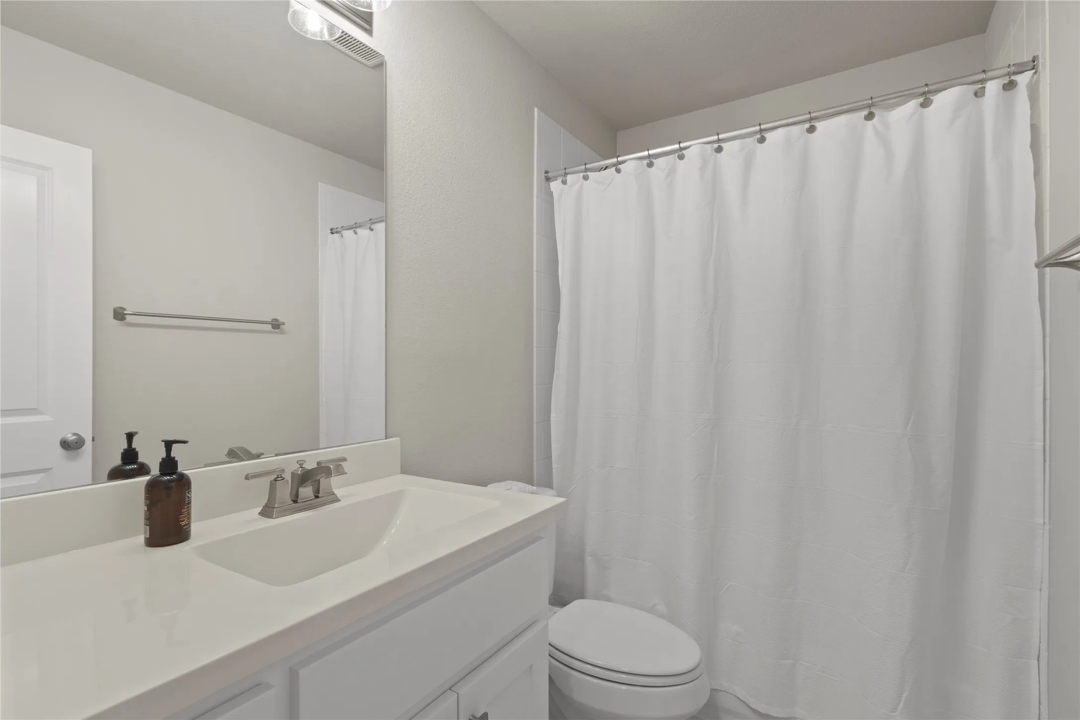 Bathroom featuring a white vanity with a solid-surface countertop, an integrated sink basin, a large wall-mounted mirror, and a tub-shower combination with a shower rod