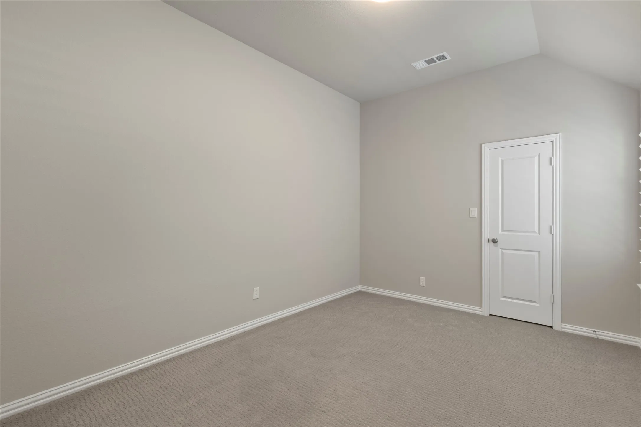 Neutral-toned interior space featuring vaulted ceilings, plush carpeting, and a two-panel interior door
